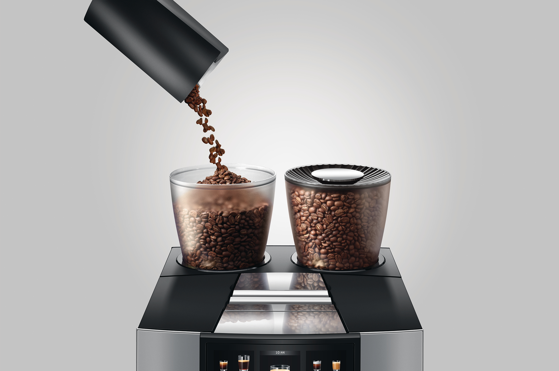 Kaffeebohnen werden in einen Glasbehälter auf einer Kaffeemaschine gegossen. Ein anderer Behälter ist voller Bohnen.