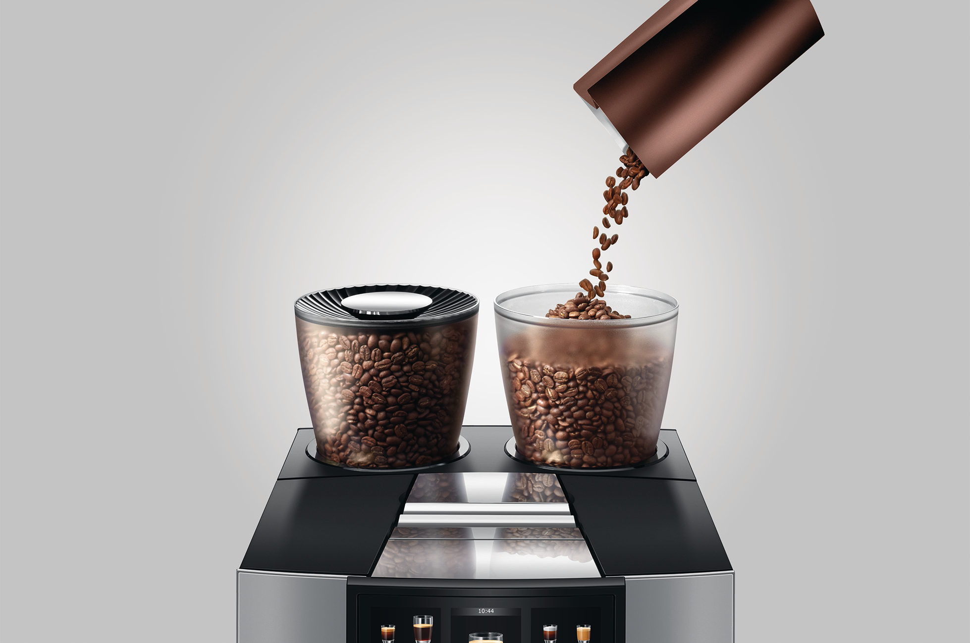 Kaffeebohnen werden in einen Glasbehälter gegossen. Zwei volle Behälter ruhen auf einer Kaffeemaschine. Braune Bohnen, hellgrauer Hintergrund.