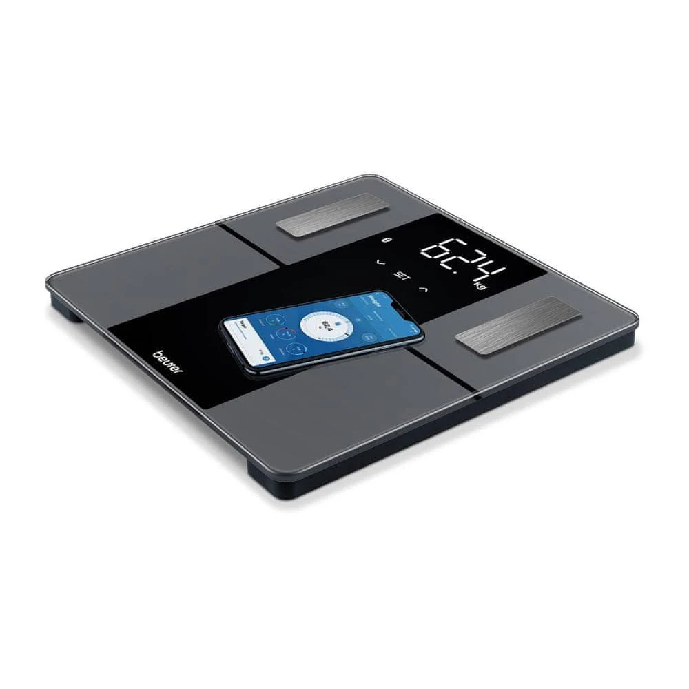 Una báscula digital con un smartphone encima. La báscula muestra 62,74 kg. El smartphone muestra una app de seguimiento de peso.