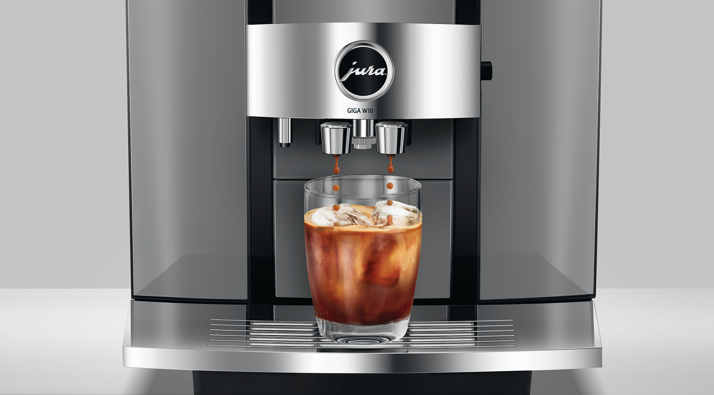 Eine Kaffeemaschine, die Kaffee in ein Glas mit Eis ausgibt. Die Maschine ist silberfarben, der Kaffee braun und der Hintergrund weiß.
