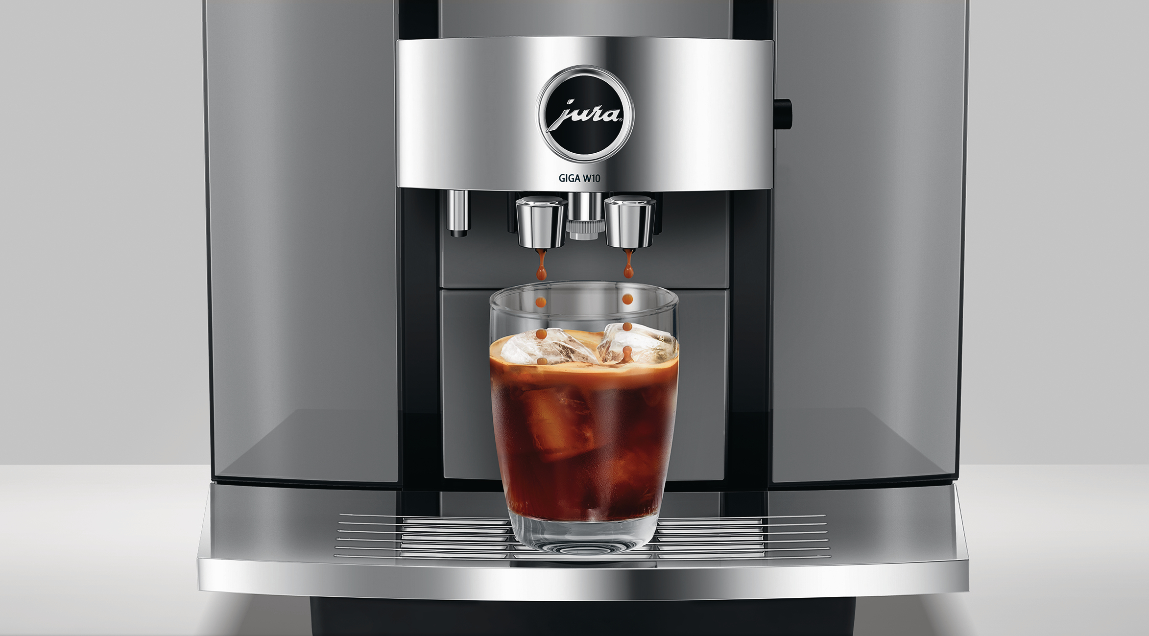 Eine Kaffeemaschine, die Kaffee in ein Glas mit Eiswürfeln ausgibt. Die Maschine hat ein Markenlogo und ist silberfarben.