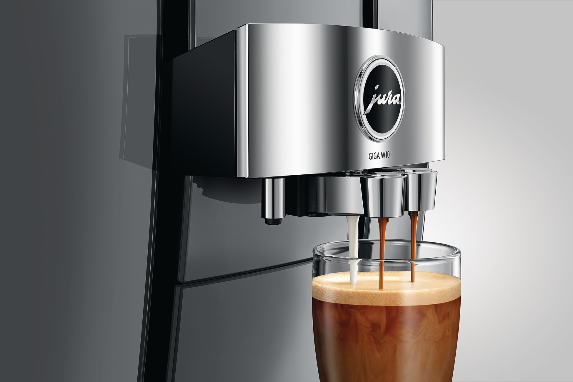 Eine silberne Jura GIGA W10 Kaffeemaschine, die Kaffee und Milch in ein Glas ausgibt. Der Kaffee hat eine schaumige Oberfläche.