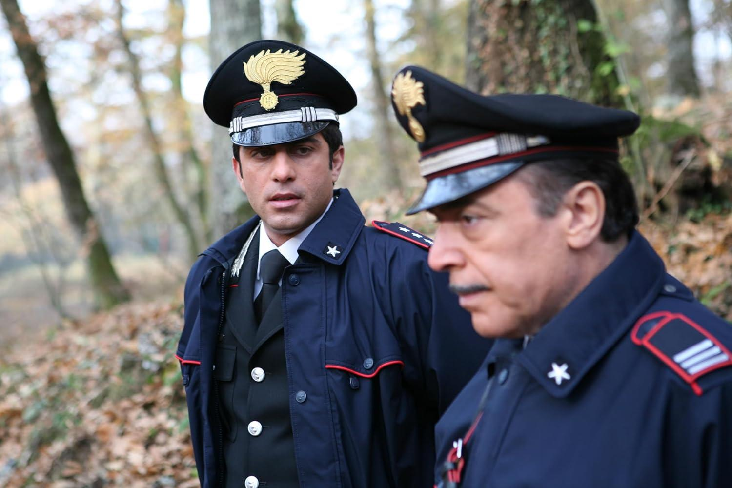 Zwei Männer in Marineuniformen mit Hüten. Einer schaut in die Kamera. Der Hintergrund ist ein Wald mit Bäumen und Laub.