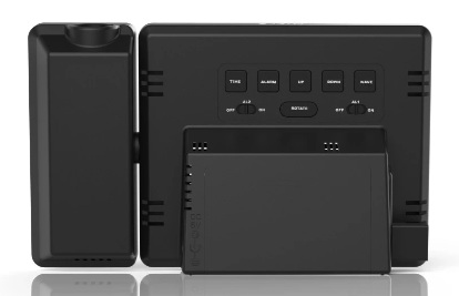 Pokazano tył czarnego zegara cyfrowego. Posiada przyciski do ustawiania czasu, alarmu, góra/dół i nawigacji. Ma również projektor i małą podstawkę.