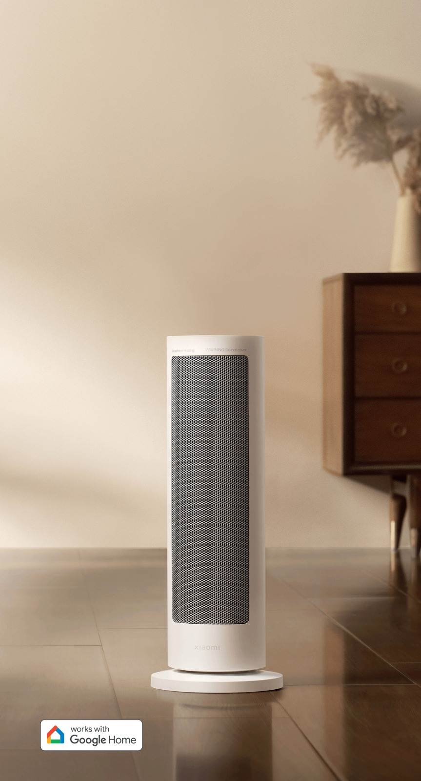 Beyaz Xiaomi ısıtıcı. Siyah ağ ön yüzü olan uzun, silindirik bir cihaz. Google Home ile çalışır. Arka planda ahşap dolap ve vazo.
