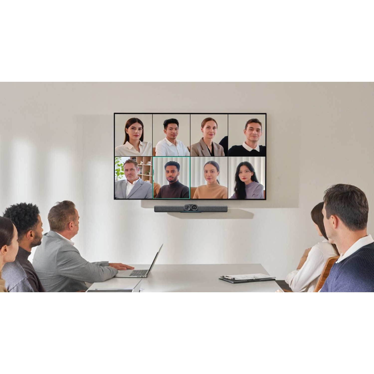 Una sala conferenze con uno schermo che mostra una videochiamata. Diverse persone sono nella stanza, alcune guardano lo schermo.