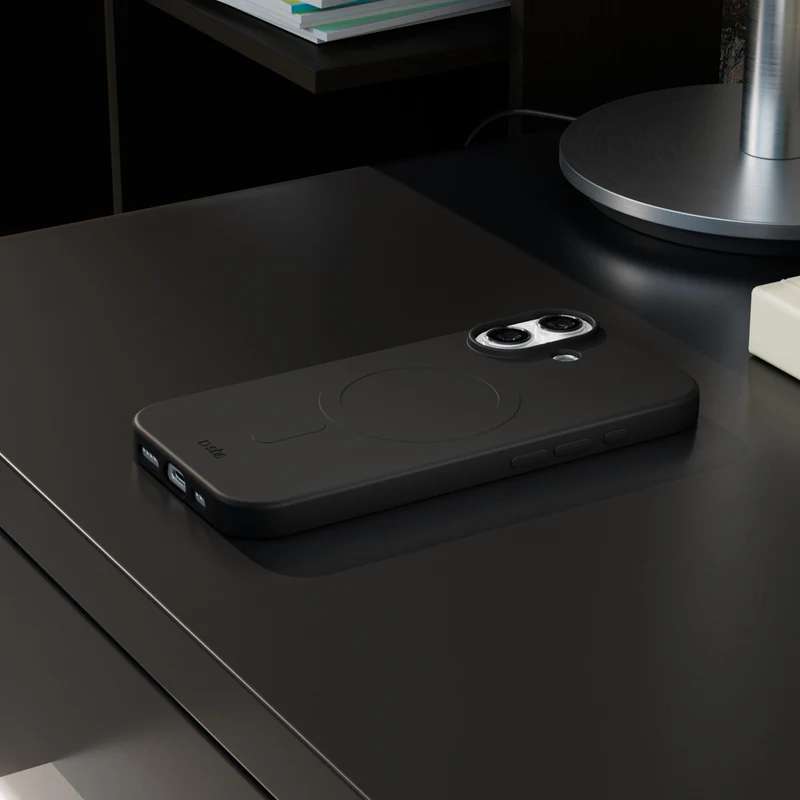 Ein schwarzes Smartphone in einer Hülle liegt auf einem schwarzen Tisch. Eine Lampe und ein Regal mit Büchern sind im Hintergrund.