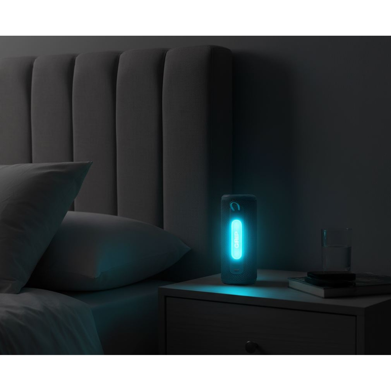 Una scena da comodino con un altoparlante blu brillante con l'etichetta 'GRIP', un letto, cuscini, un comodino, un bicchiere e un libro.