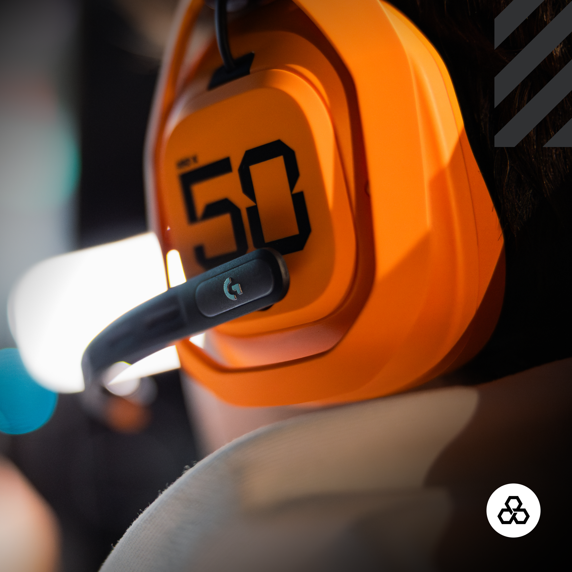 Egy narancssárga gamer headset, rajta az 50-es számmal, fekete mikrofonnal és logóval. A háttér sötét.