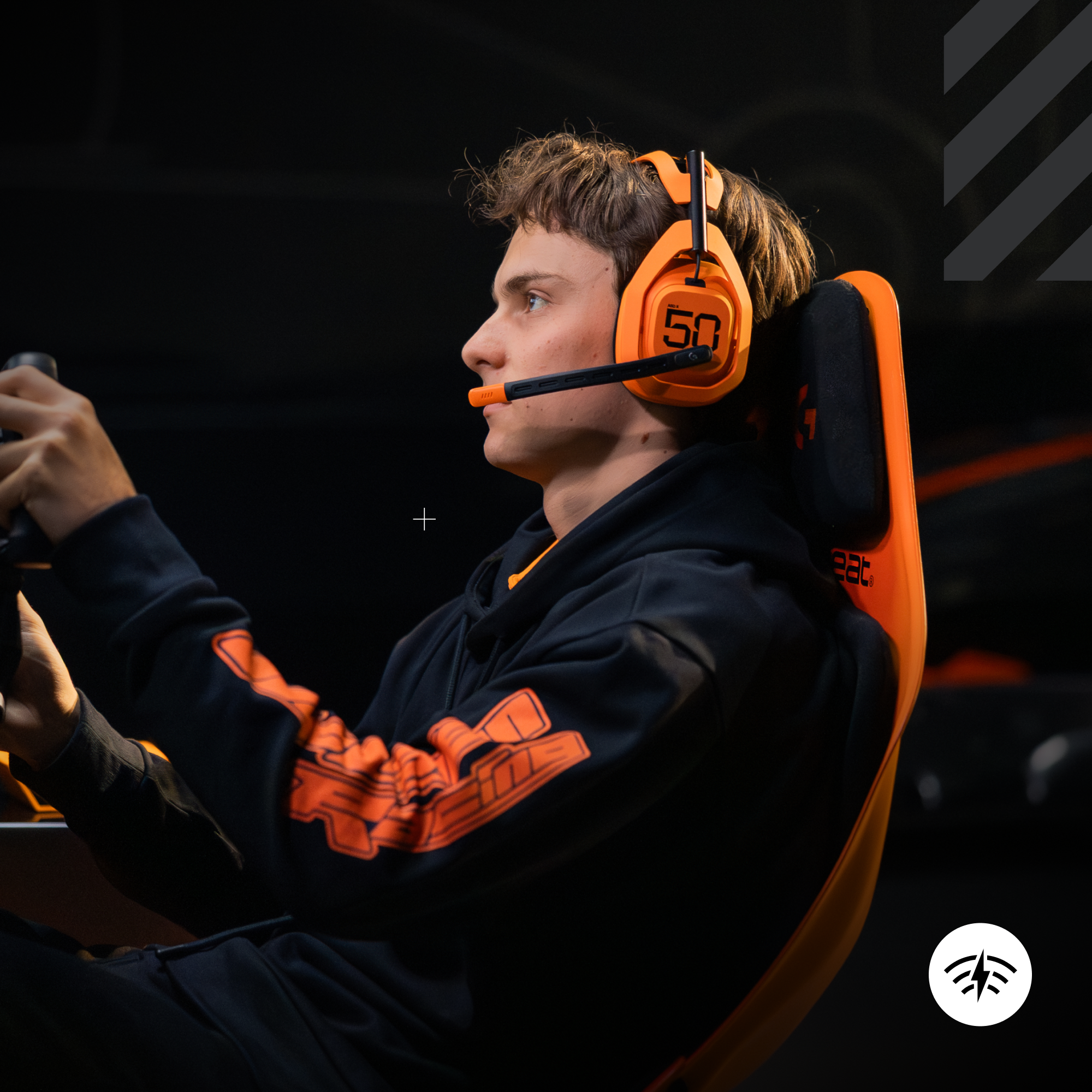 Egy narancssárga fejhallgatót és fekete kapucnis pulóvert viselő személy egy gamer székben ül. A kontrollerre koncentrál.