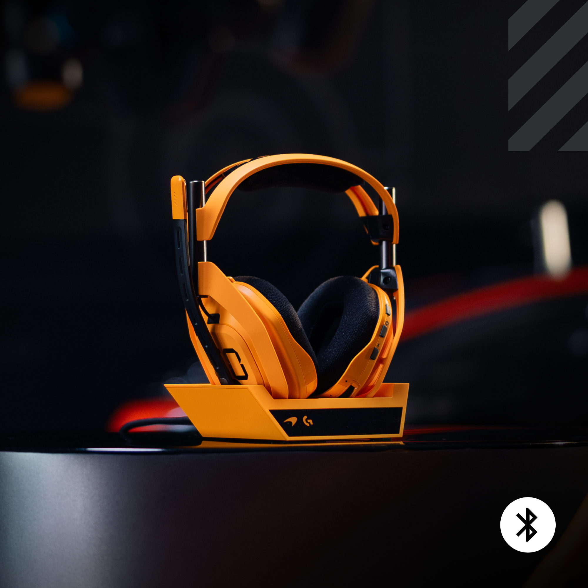 Narancssárga gamer fejhallgató fekete állványon. Fekete fülhallgatók, fekete háttér. Bluetooth szimbólum a sarokban.