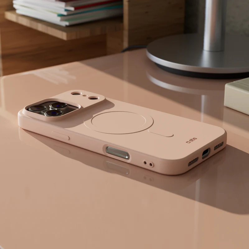 Eine rosa Handyhülle mit rundem MagSafe-Design liegt auf einer passenden Oberfläche. Die Szene umfasst einen Schreibtisch und eine Lampe.
