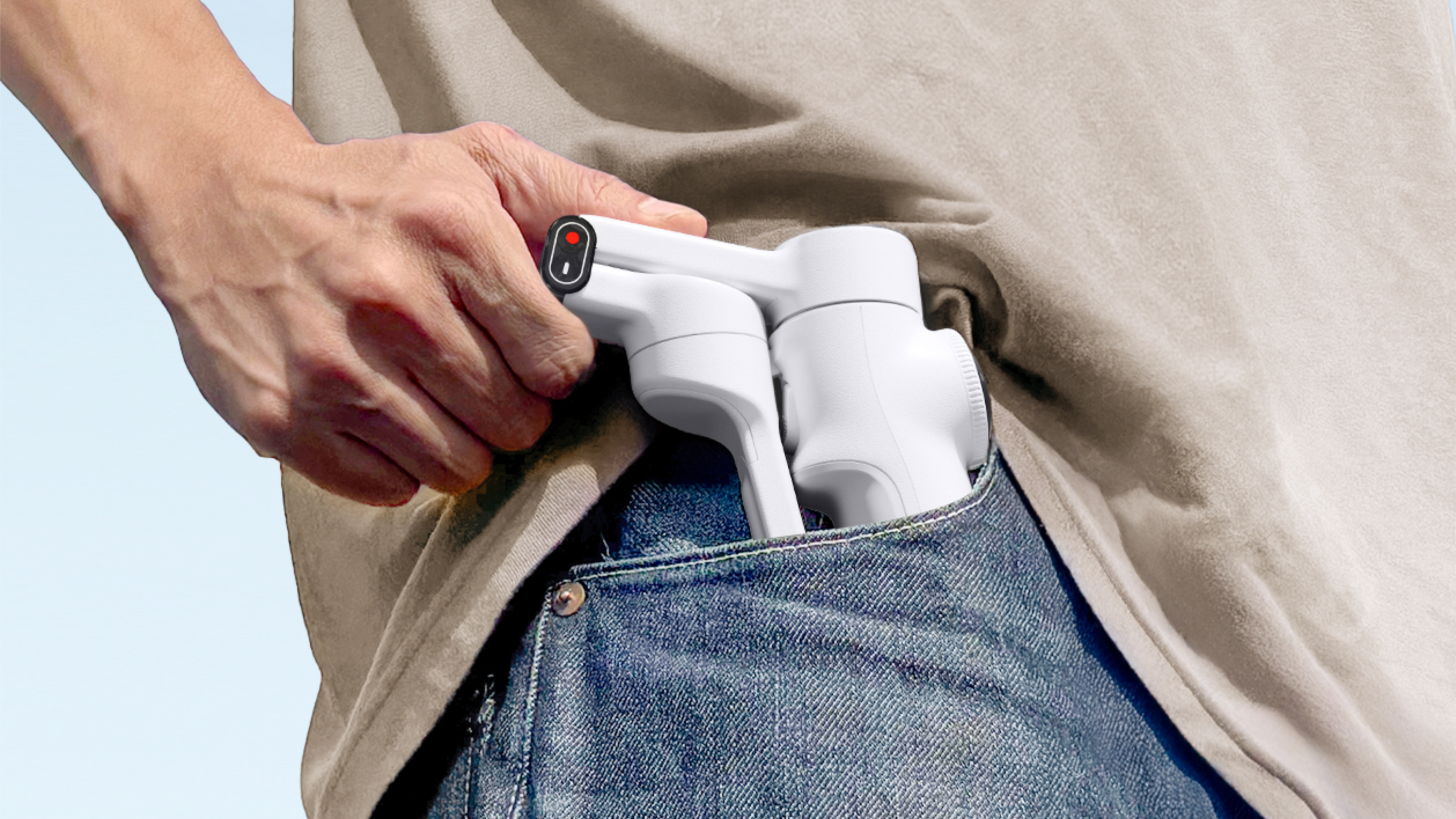 Eine Hand steckt einen weißen Gimbal-Stabilisator in eine blaue Jeanstasche. Die Person trägt ein beiges Hemd.