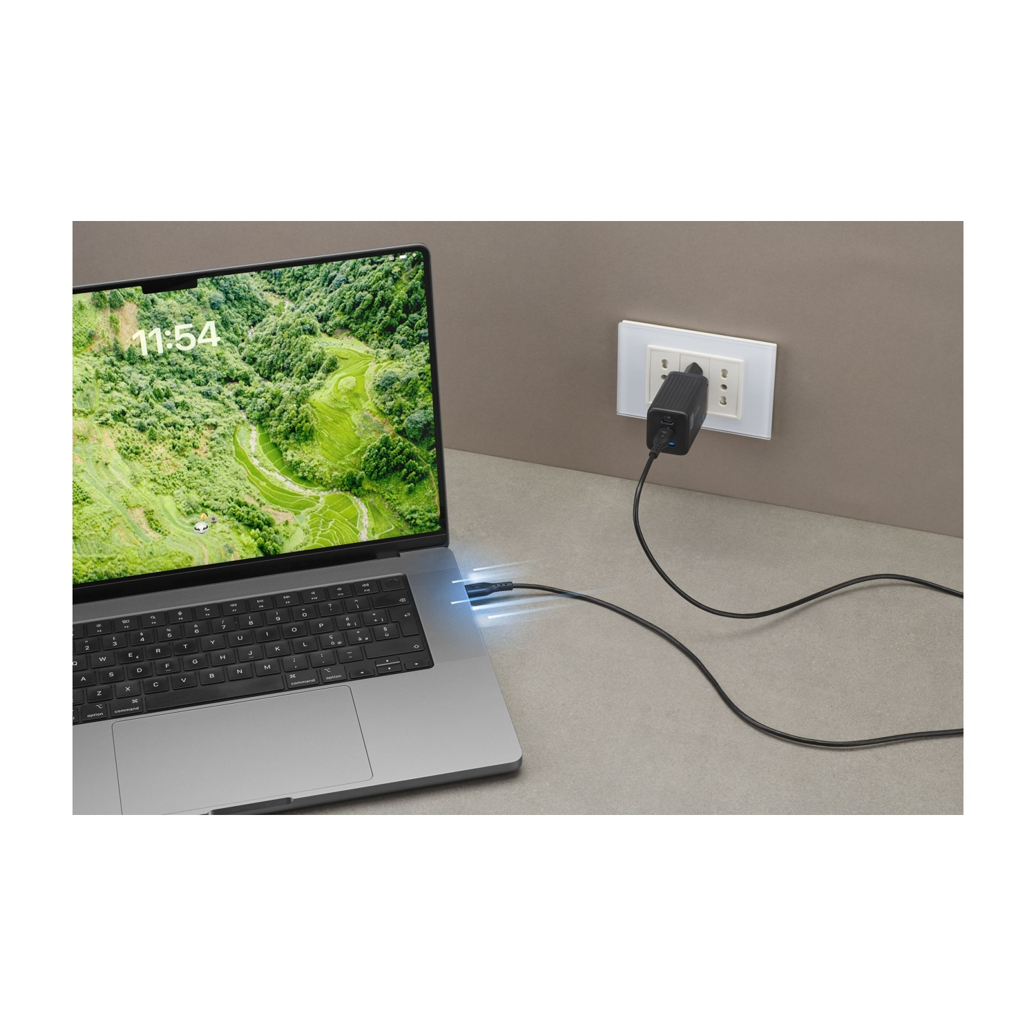 Laptop collegato al caricatore. Lo schermo mostra un paesaggio verde. Il caricatore è collegato alla presa a muro.