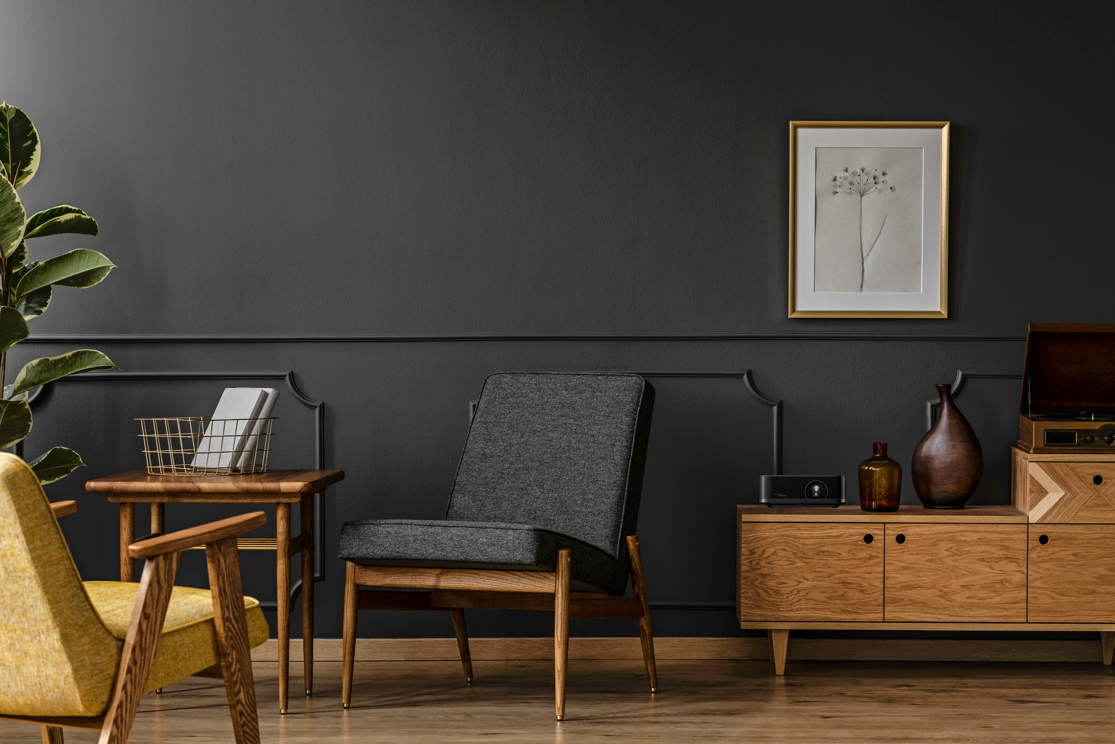 Wohnzimmer mit dunklen Wänden, Holzmöbeln und einem goldgerahmten Bild. Enthält eine Pflanze, Stühle und einen Plattenspieler.