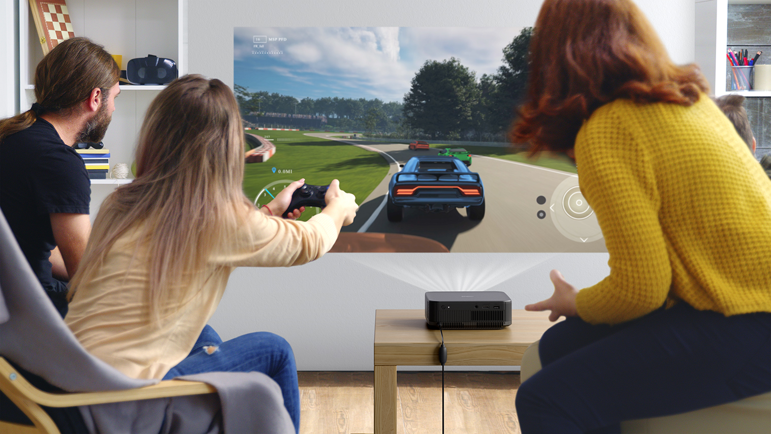 Leute spielen ein Rennvideospiel auf einem großen Bildschirm. Ein blaues Auto steht im Mittelpunkt. Ein Projektor steht auf einem Tisch.