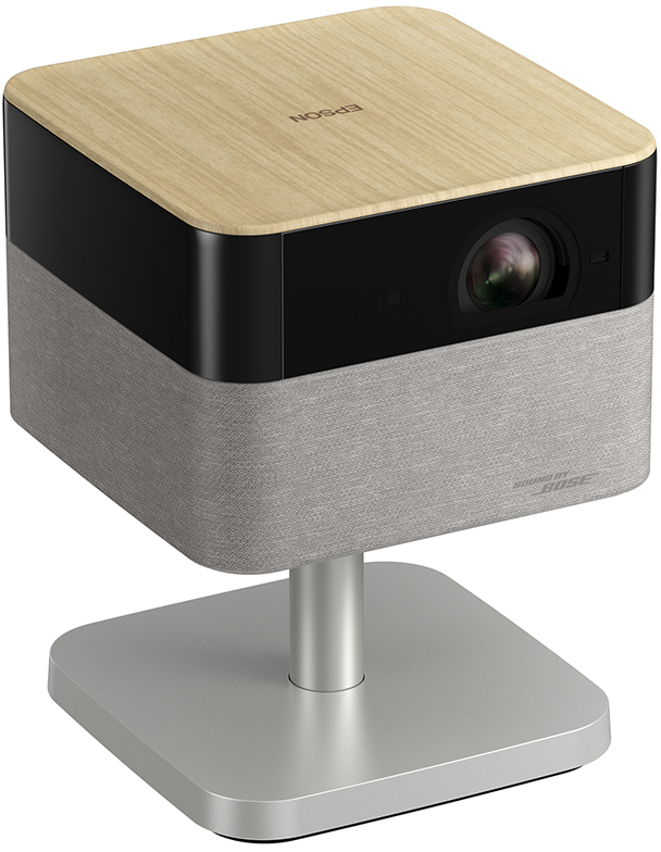 Ein Projektor auf einem Ständer. Er hat eine Holzoberseite, einen schwarzen Mittelteil und einen grauen Stoffboden. Er ist mit Epson und Bose versehen.