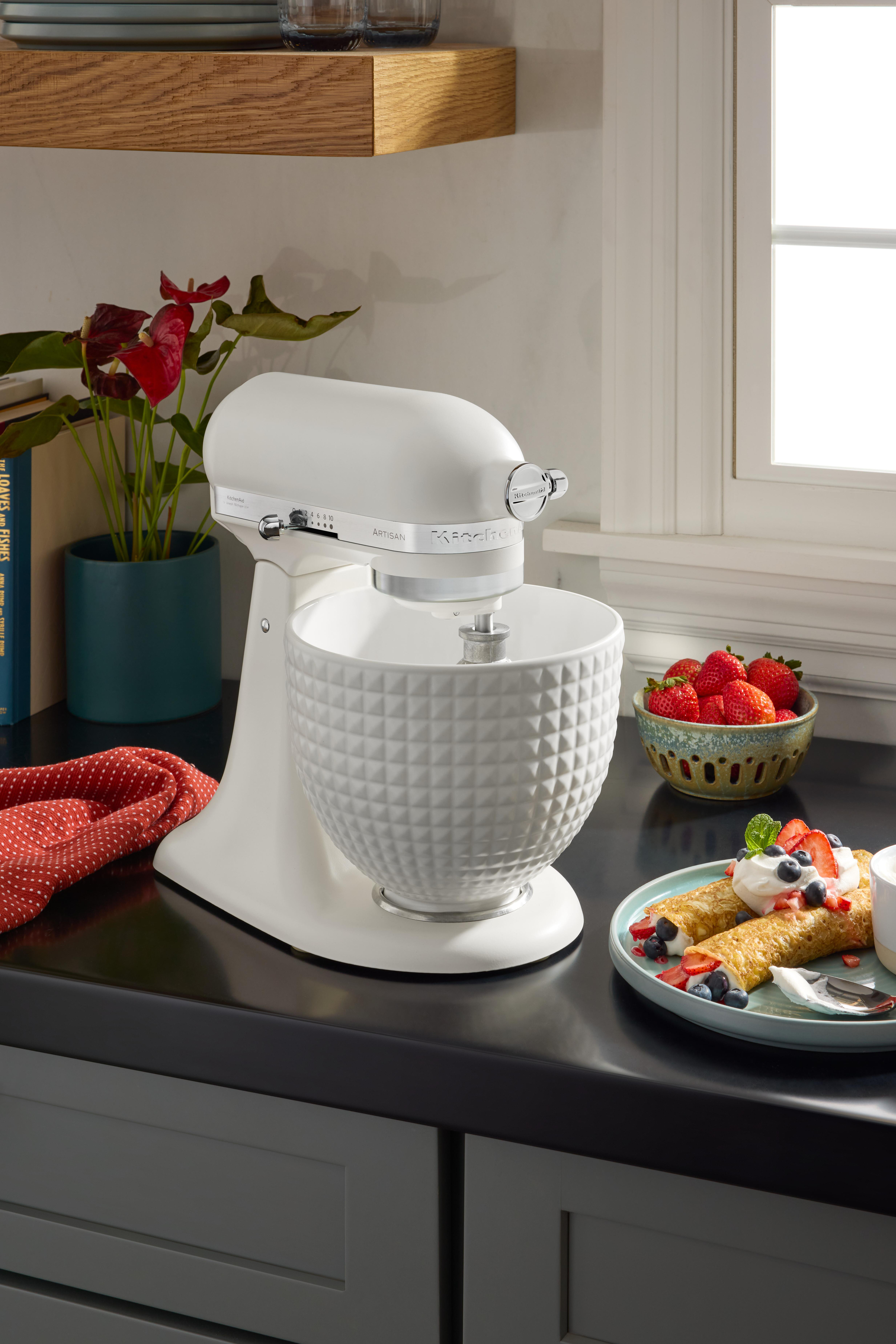 Ein weißer Küchenmixer auf einer Theke mit Desserts und Erdbeeren. Anthurium-Pflanzen in einem Topf sind links.