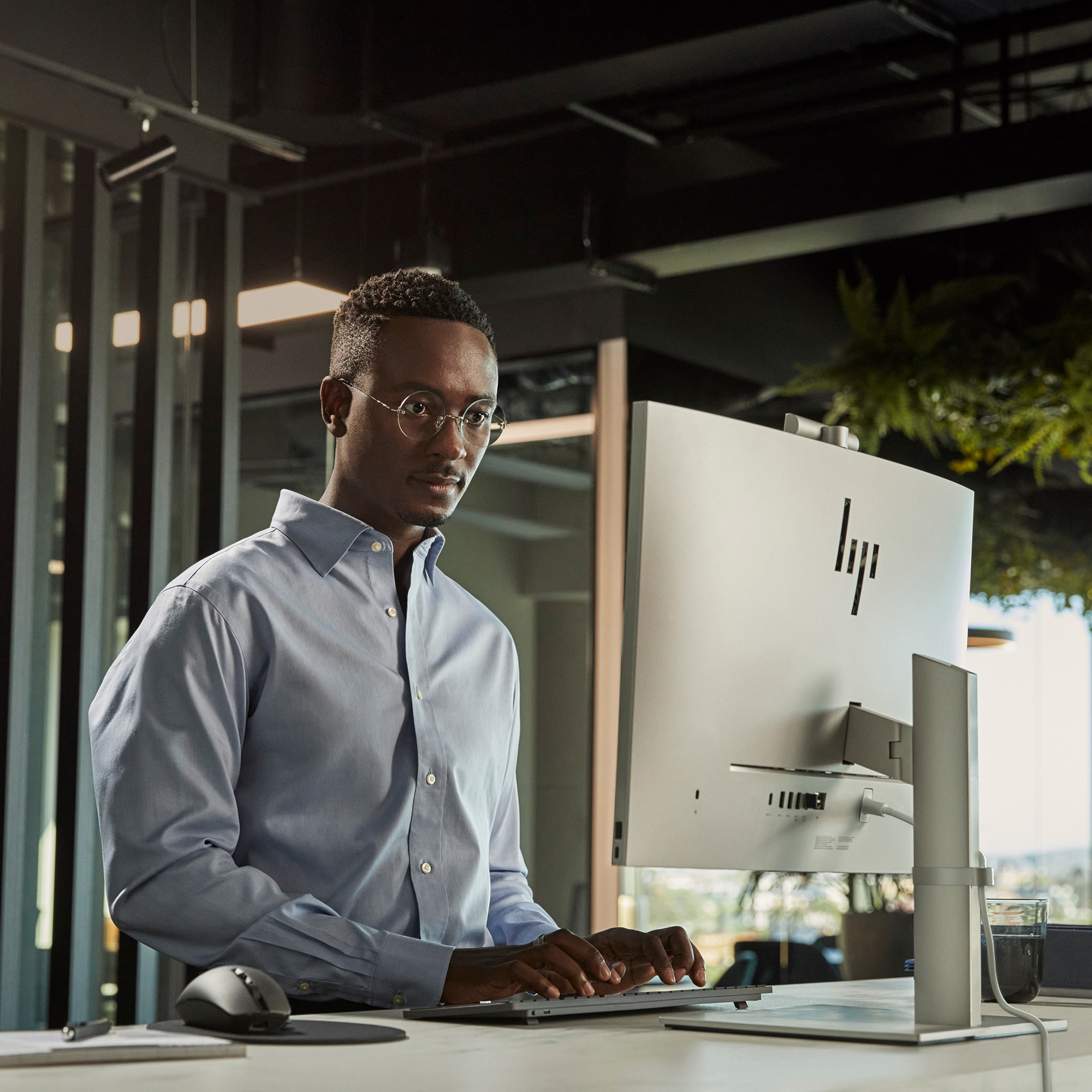 Ein Mann mit Brille tippt vor einem HP-Monitor auf einer Tastatur. Er befindet sich in einem Büro.