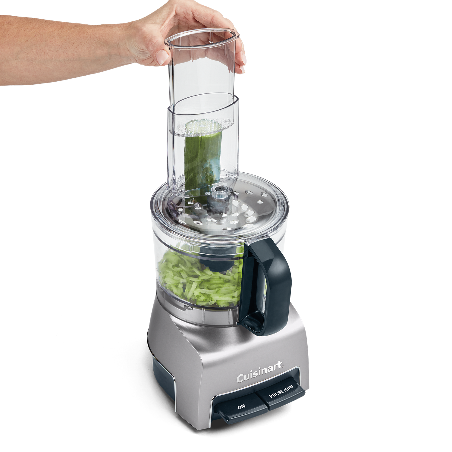 A person is using a Cuisinart food processor. A cucumber is being inserted. Shredded cucumber is in the bowl.