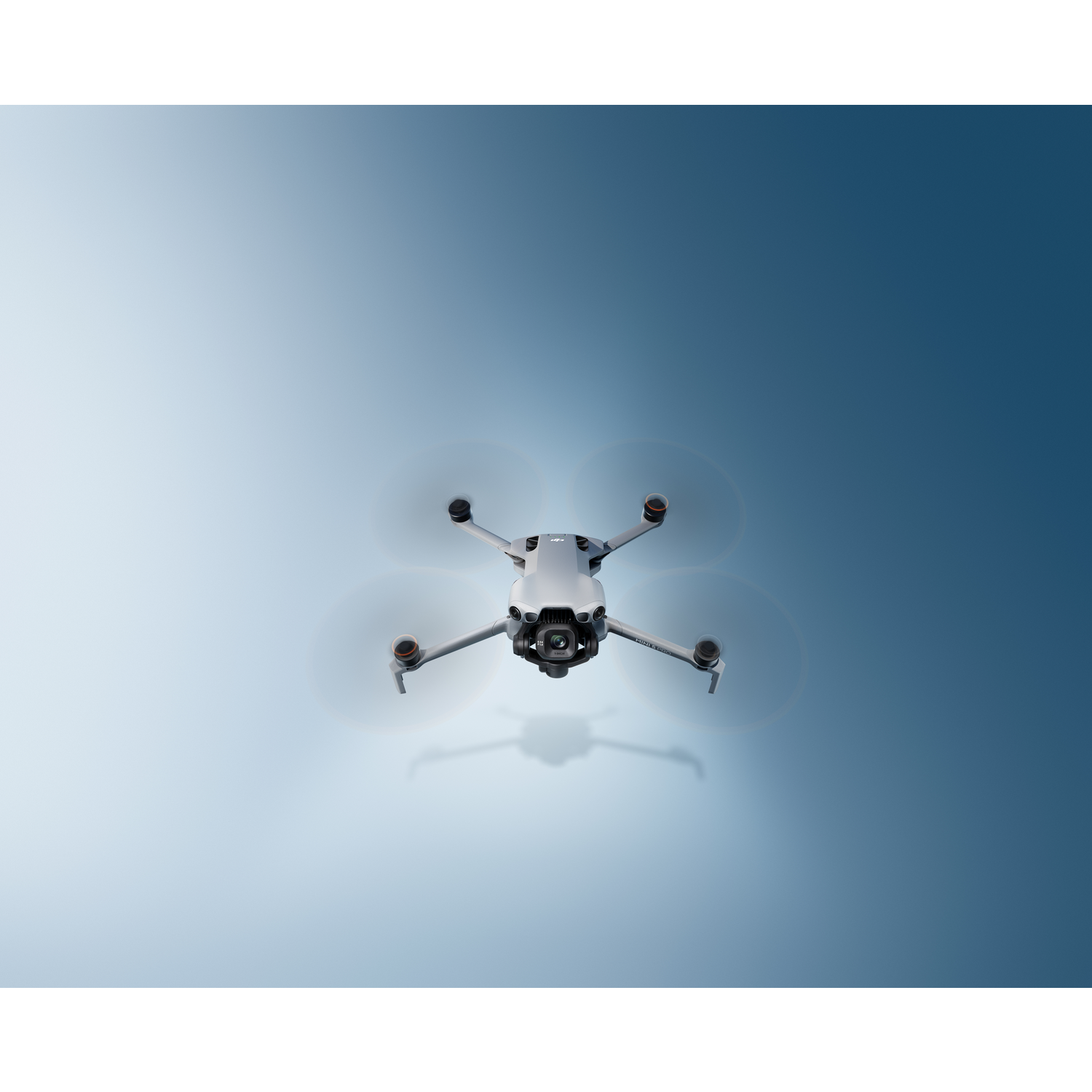 A gray drone with spinning propellers hovers against a gradient blue sky. The drone's shadow is visible below it.