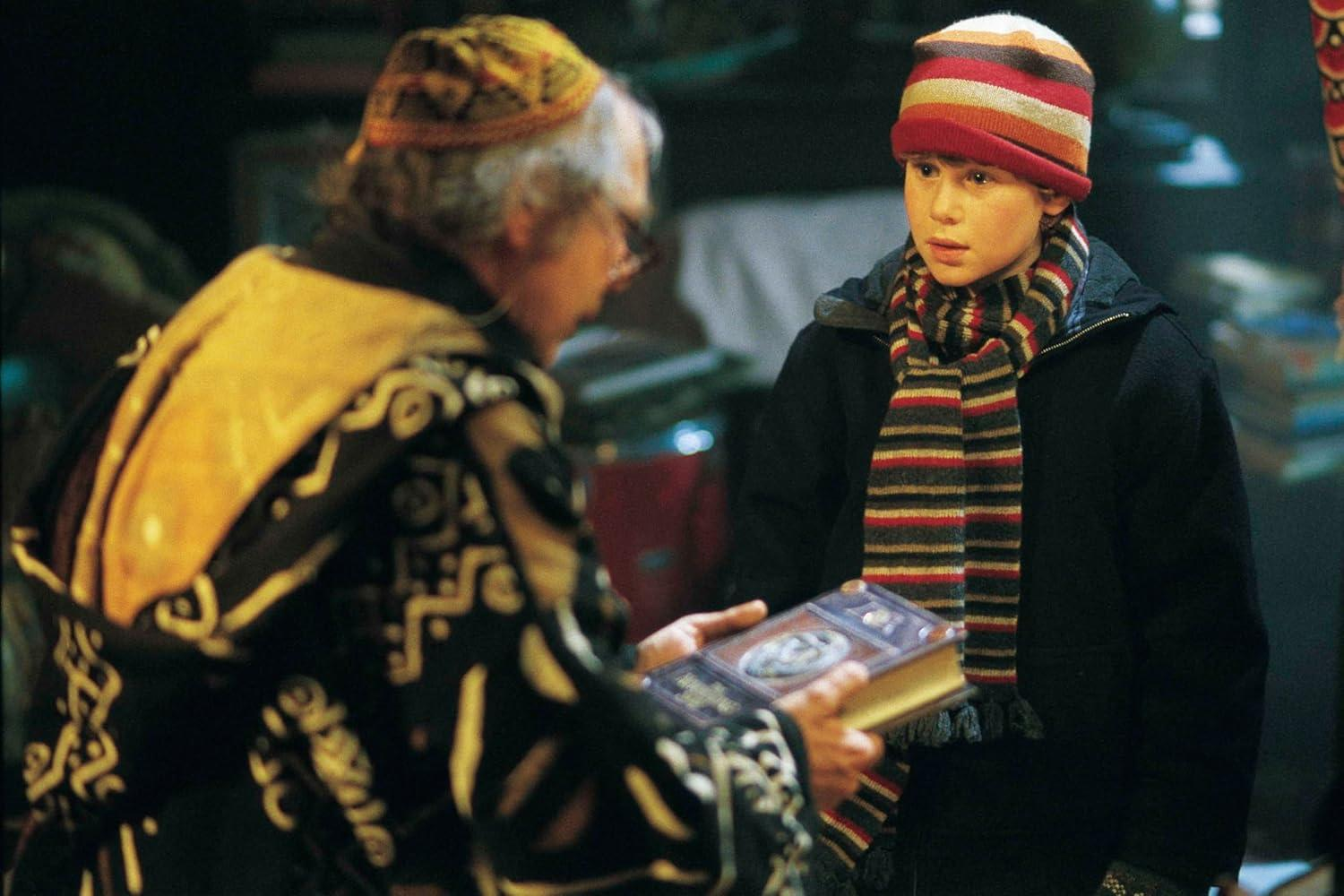 Eine ältere Person gibt einem Jungen mit gestreifter Mütze und Schal ein Buch. Der Junge betrachtet das Buch aufmerksam.