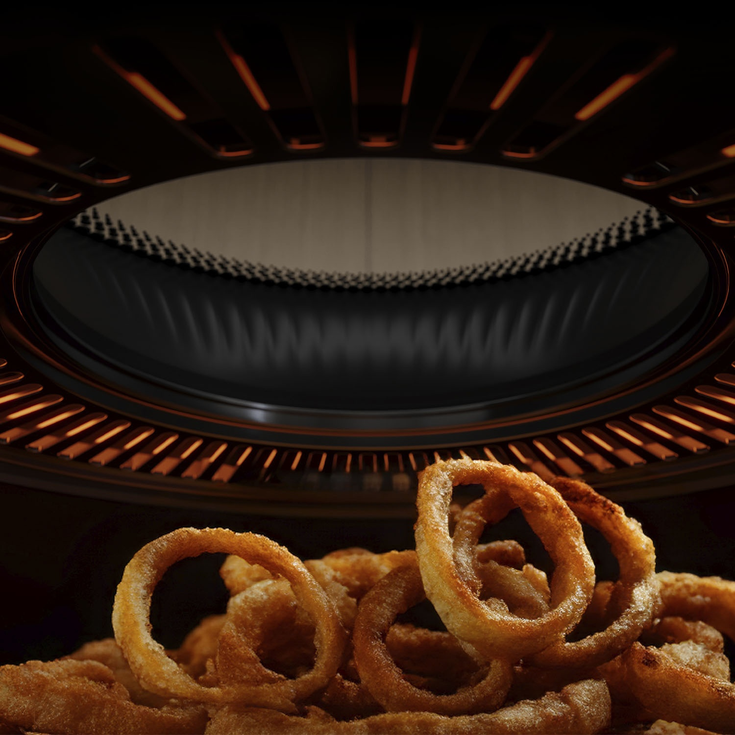 Primo piano di anelli di cipolla fritti, dorati, davanti all'interno scuro di un forno. Il forno ha un design circolare con luci.