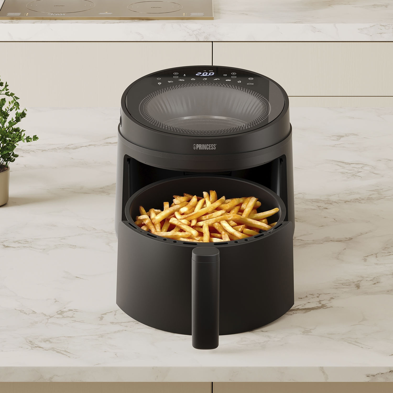 Una friggitrice ad aria nera con patatine fritte. Si trova su un piano di lavoro in marmo. Una pianta e un piano cottura sullo sfondo.
