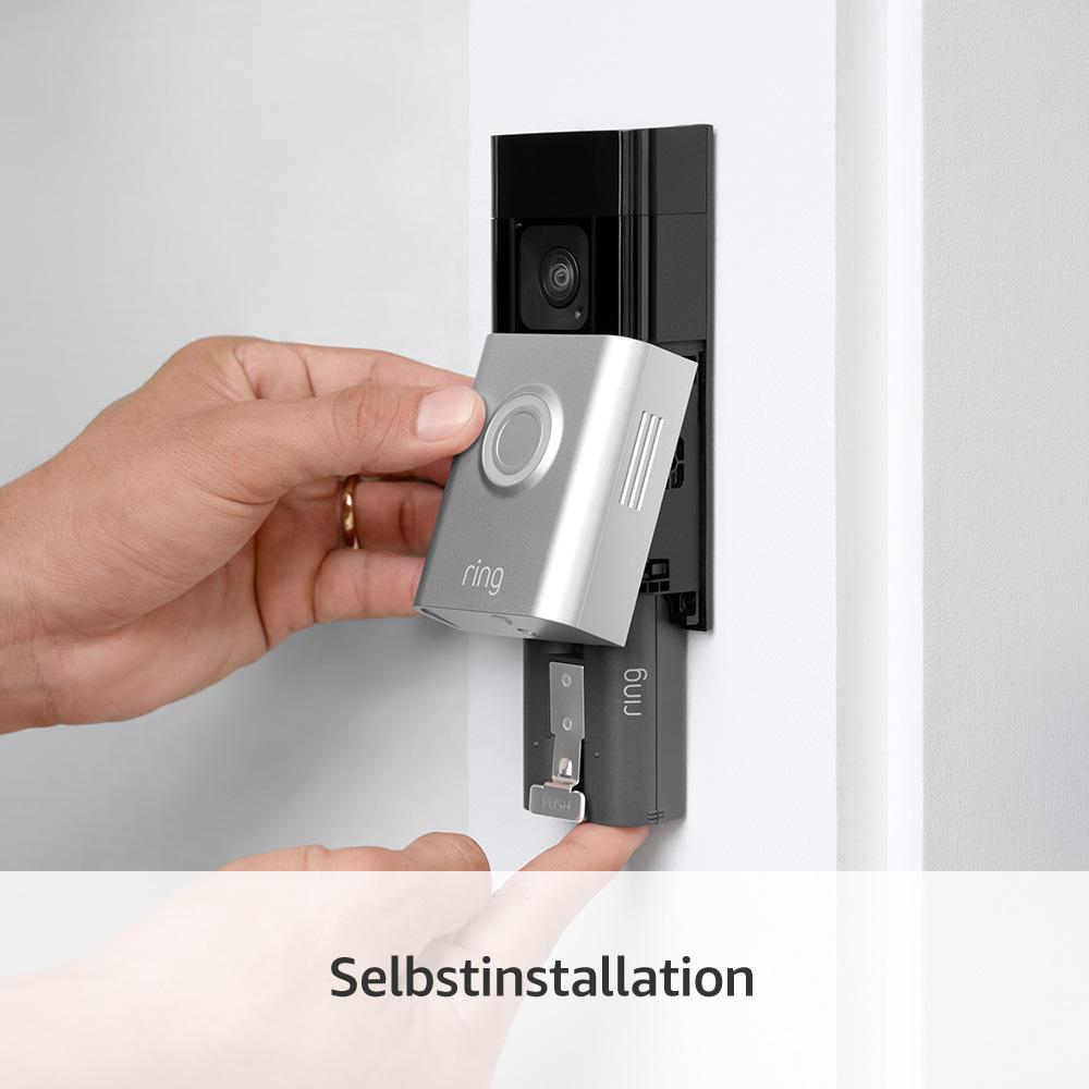 Person installiert eine Ring-Türklingel. Die silberne Türklingel wird an ihrer schwarzen Basis an einer weißen Wand befestigt.