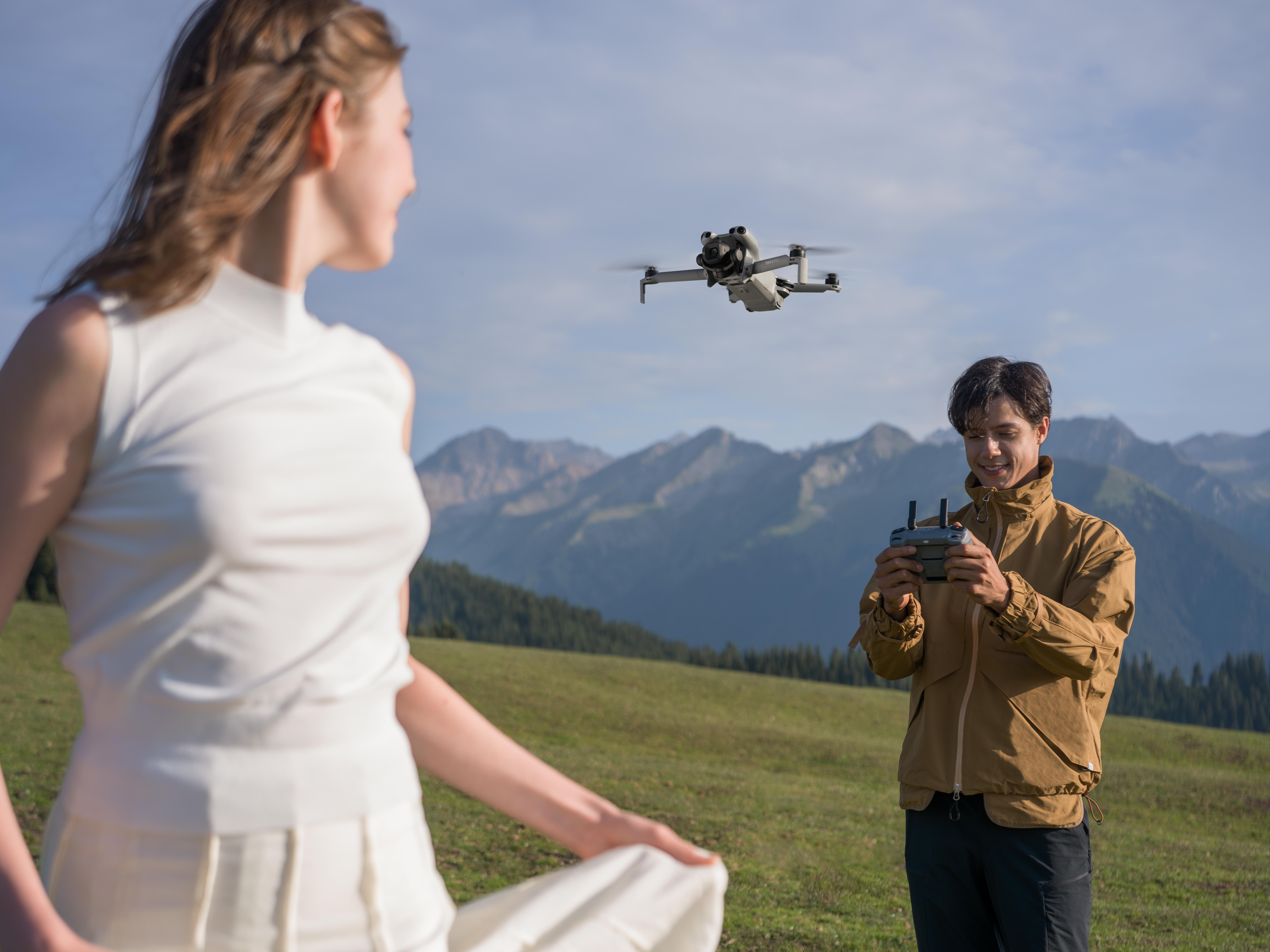 Eine Frau und ein Mann mit einer Drohne. Der Mann hält eine Fernbedienung. Berge sind im Hintergrund.