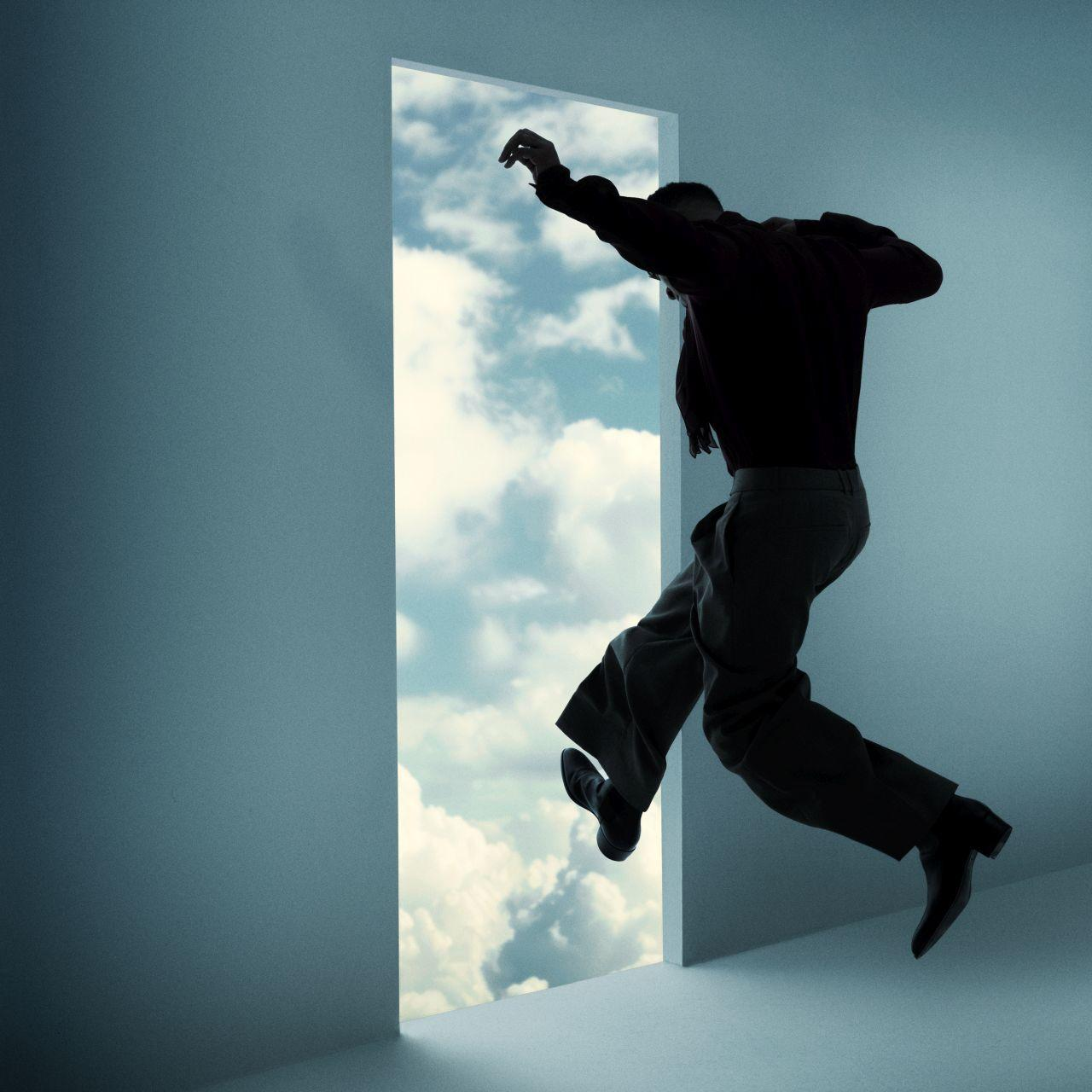 Eine Person in dunkler Kleidung springt durch eine Tür in einen bewölkten Himmel.