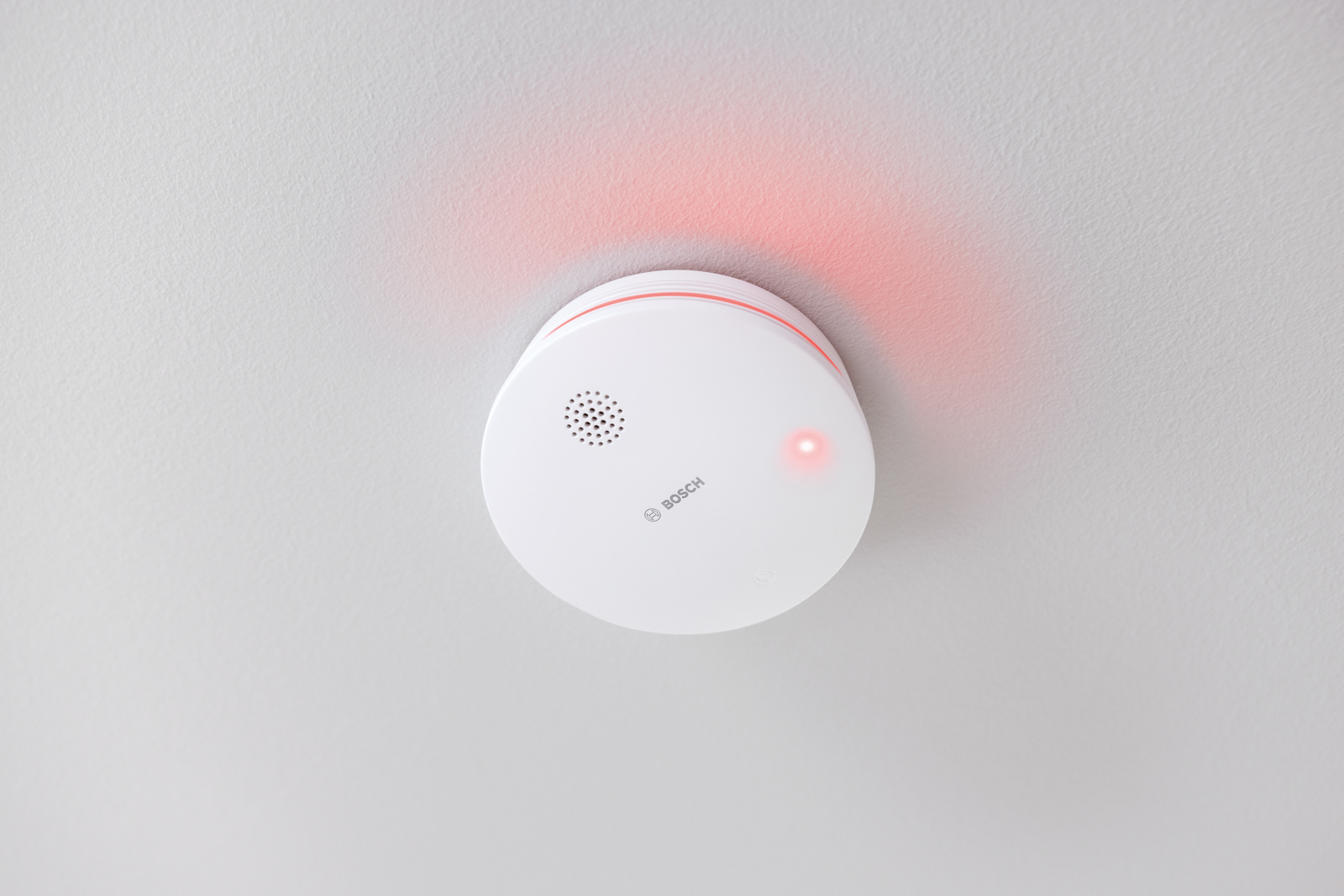 Ein weißer Bosch-Rauchmelder ist an einer weißen Decke montiert. Er hat ein rotes Licht, das den aktiven Zustand anzeigt.