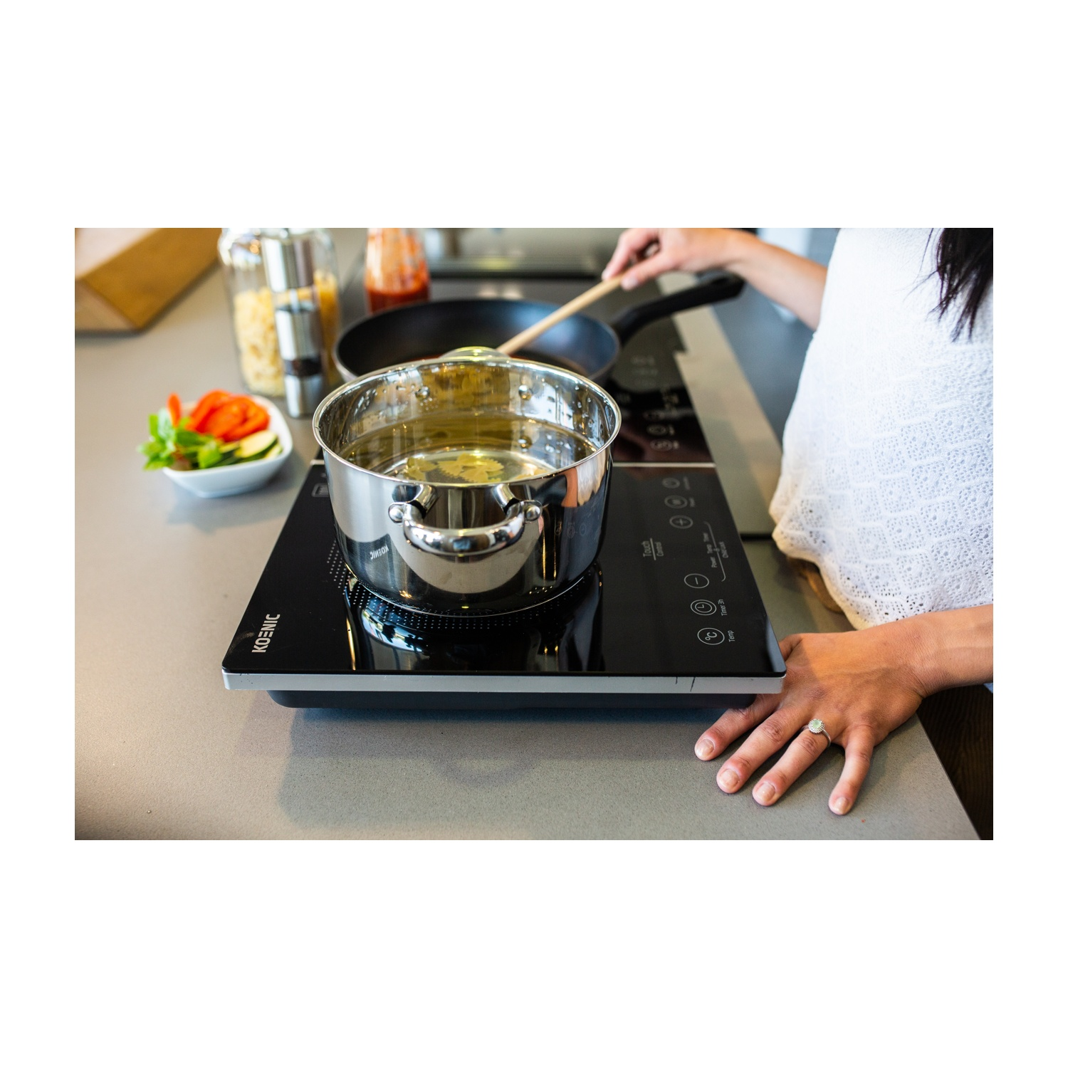 Una persona cucina in cucina. Una pentola con acqua è su un fornello nero. Verdure in un piatto. Una padella sul fornello posteriore.