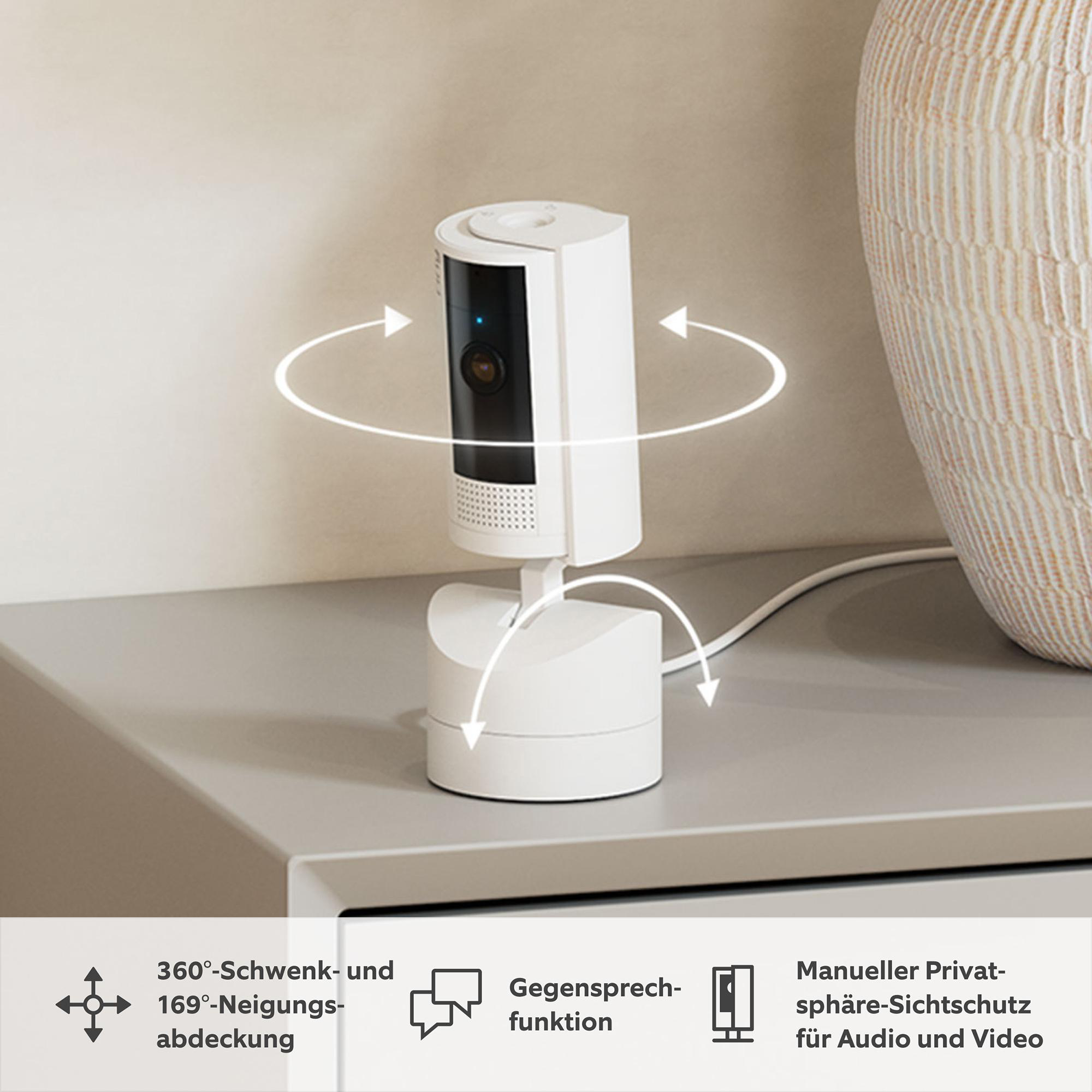 Eine weiße Überwachungskamera auf einer grauen Oberfläche, mit Pfeilen, die eine 360°-Drehung anzeigen. Eine beige Vase im Hintergrund.