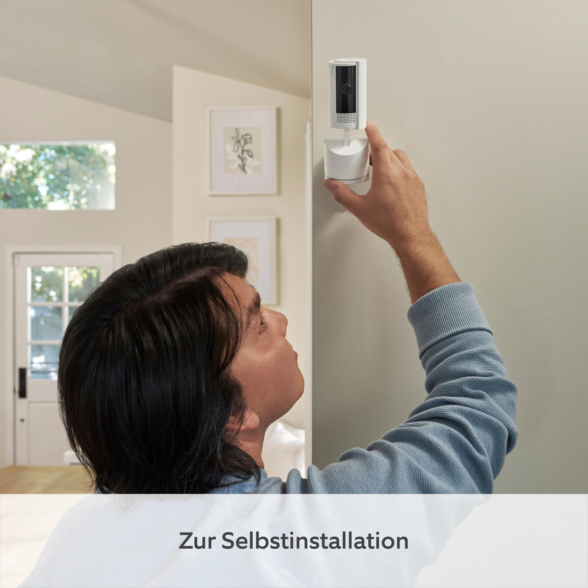 Mann installiert Überwachungskamera an der Wand. Er trägt ein blaues Hemd. Die Kamera ist weiß.