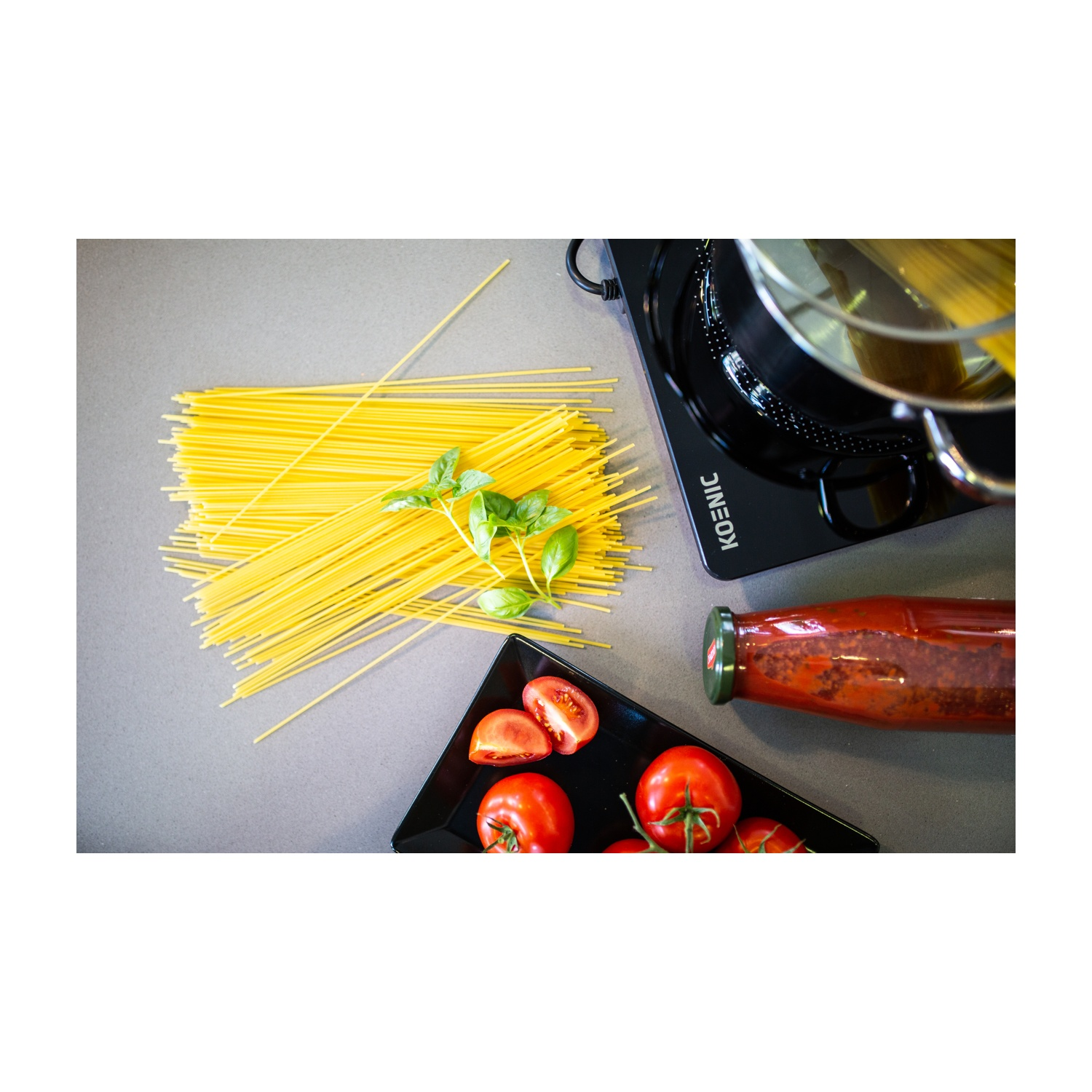 Vista dall'alto di spaghetti, basilico, pomodori e salsa accanto a una pentola su un fornello nero. Ingredienti per un pasto.
