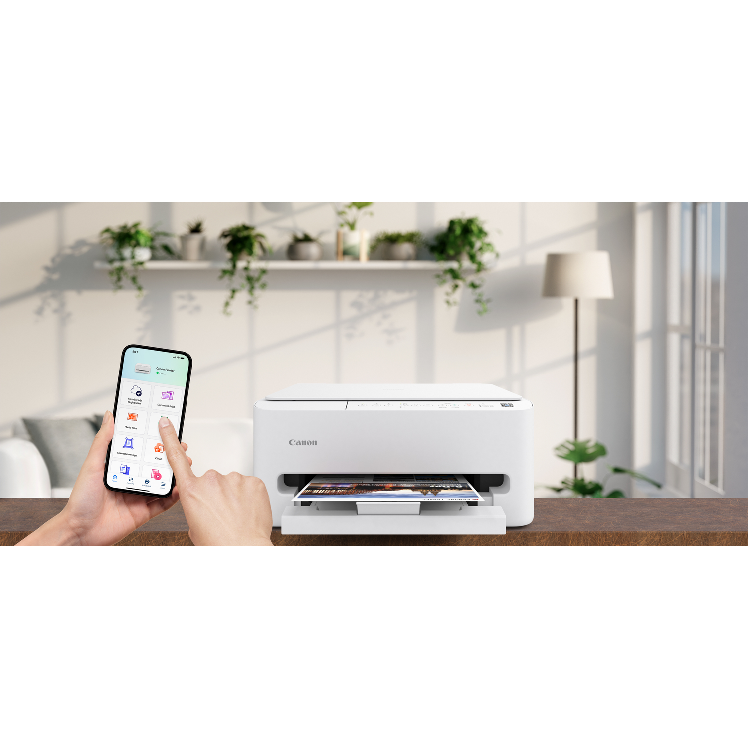 Een witte Canon-printer print een foto, bestuurd via een telefoon. Planten en een lamp staan op de achtergrond, op een houten tafel.