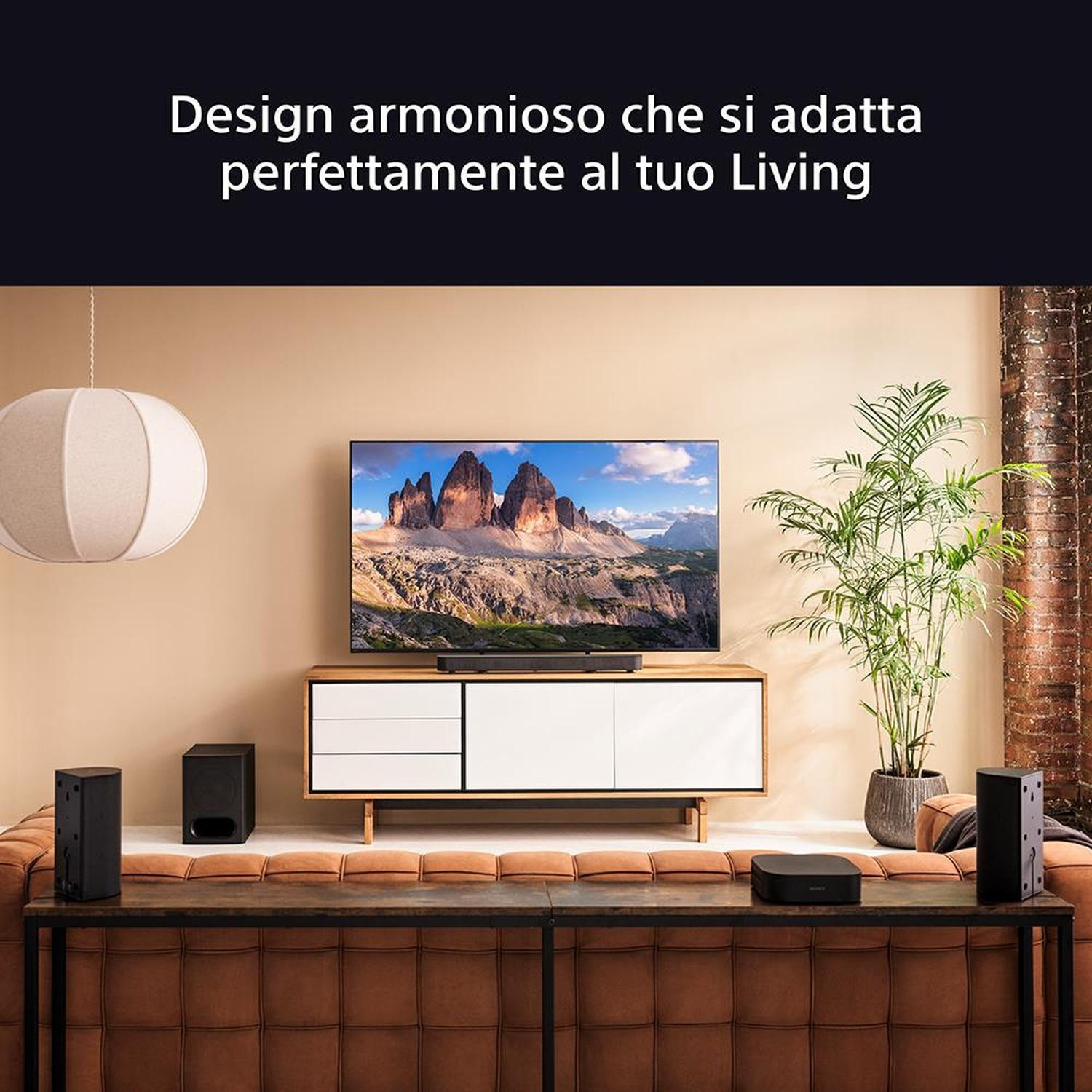 Soggiorno con TV, impianto audio e divano. Montagne sullo schermo. Sono presenti altoparlanti e una pianta decorativa.