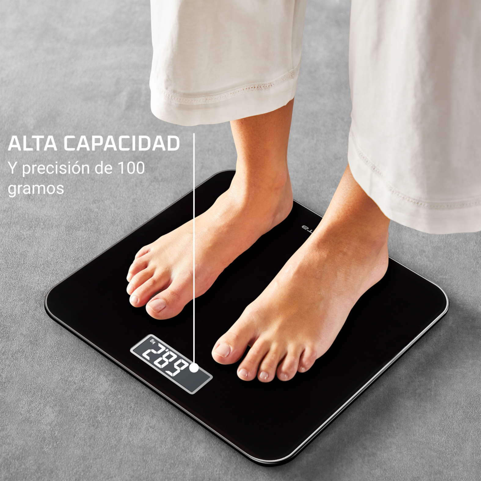 Pies sobre una báscula digital negra. La pantalla muestra 28,9 kg. Persona con pantalón blanco de pie sobre la báscula.