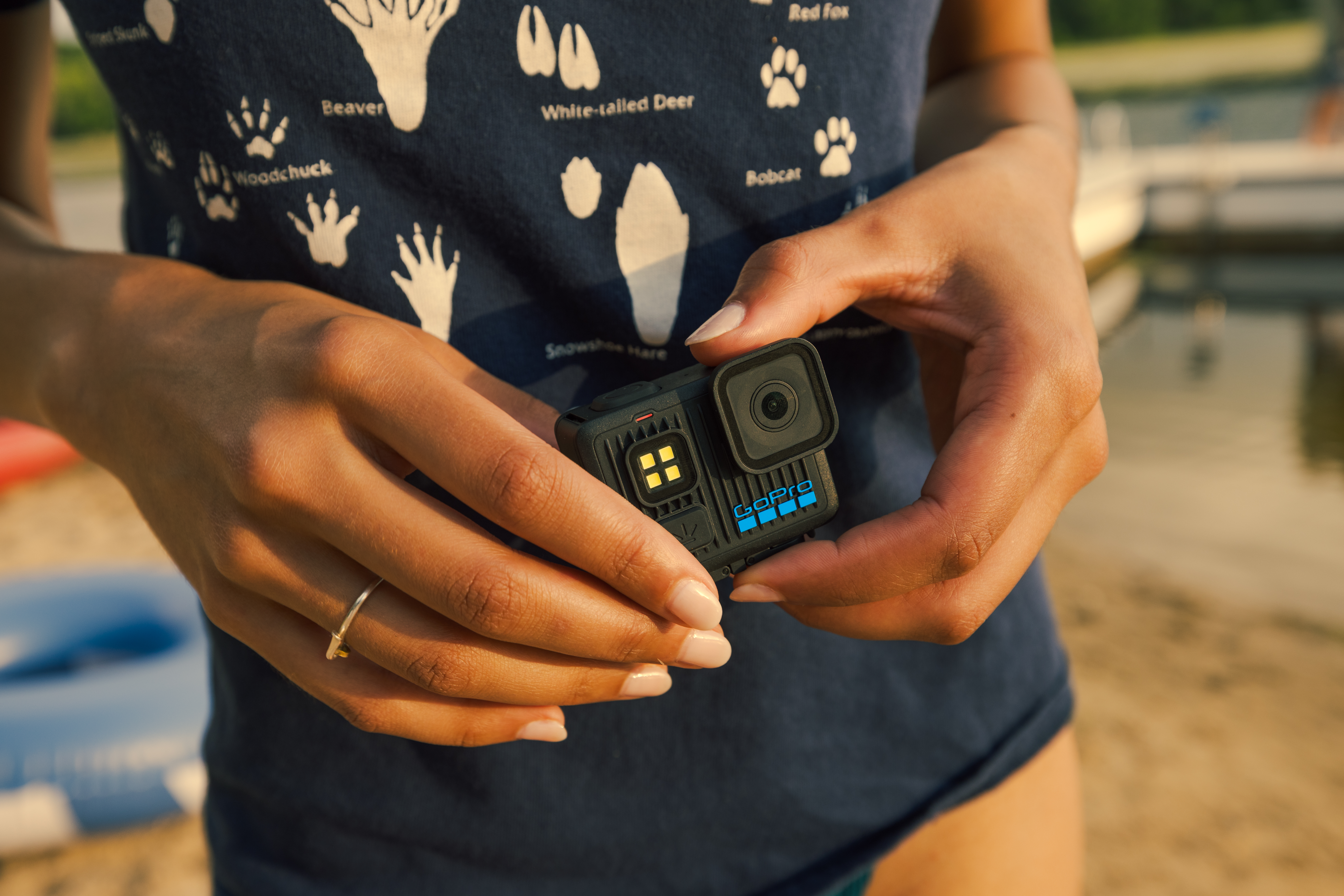 Eine Person hält eine GoPro-Kamera. Die Kamera ist schwarz mit blauen Akzenten. Die Person trägt ein blaues Hemd.
