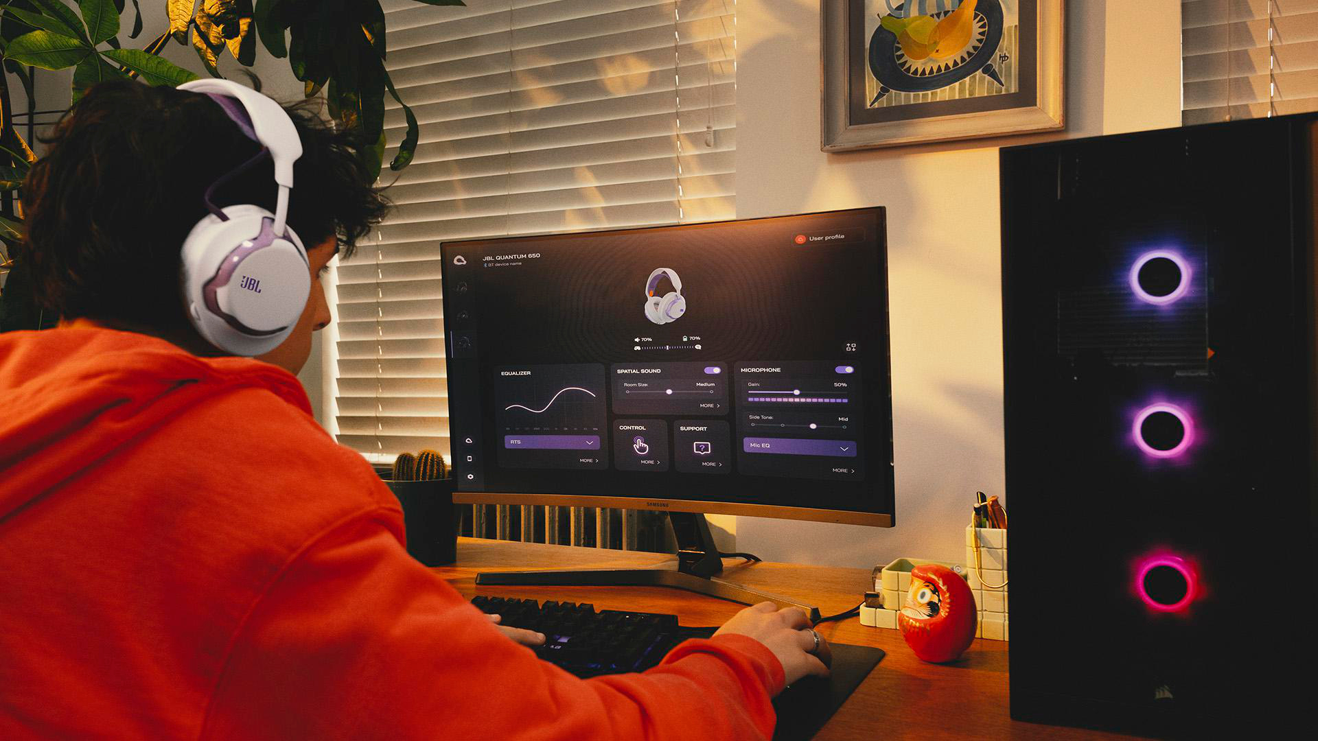 Eine Person mit JBL-Kopfhörern, die einen Computer benutzt. Ein Monitor zeigt Kopfhörereinstellungen. Ein Computerturm mit Lichtern befindet sich rechts.