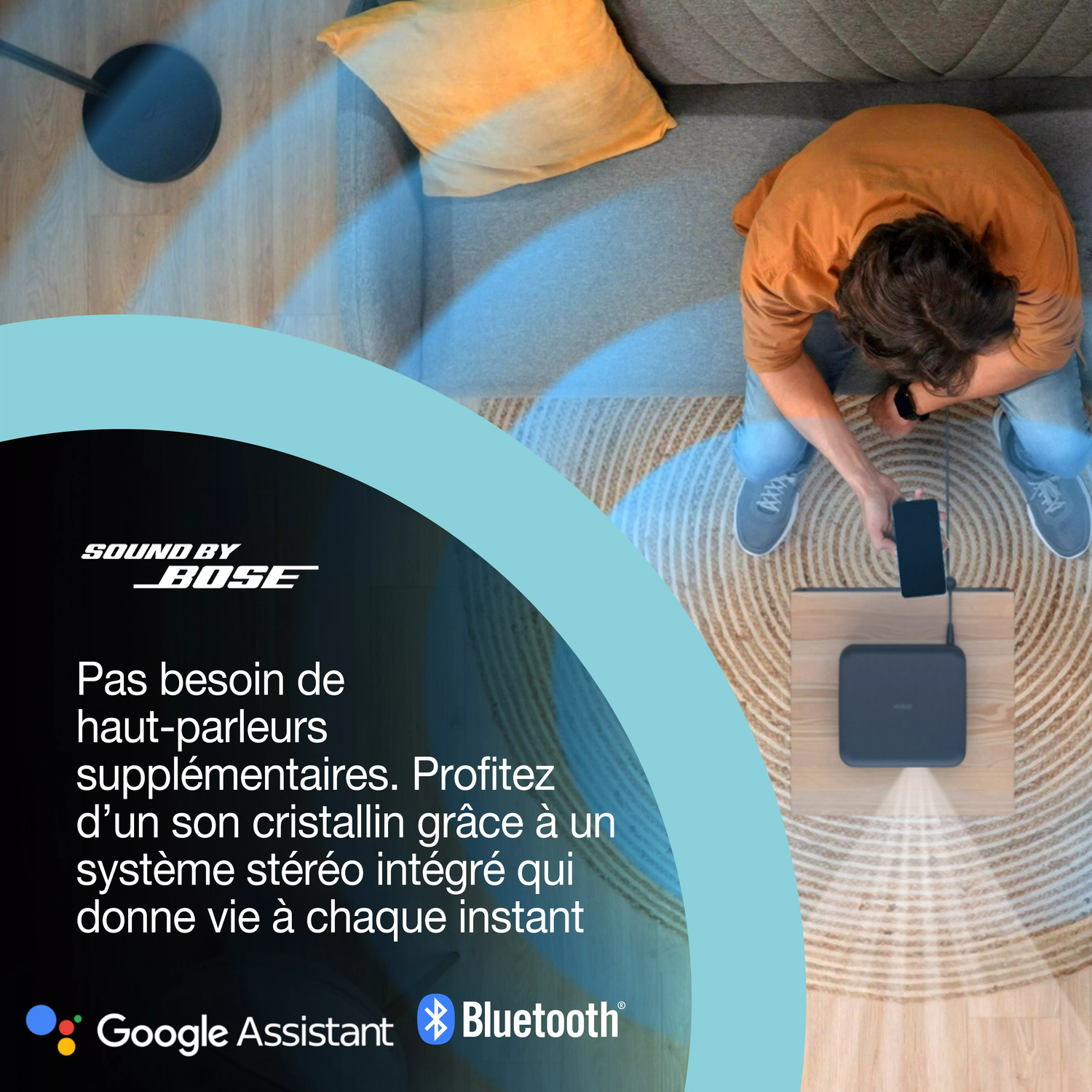 Homme assis près d'un système audio Bose, connectant un téléphone. Canapé, oreiller et tapis en arrière-plan. Texte dit 'Sound by Bose'.