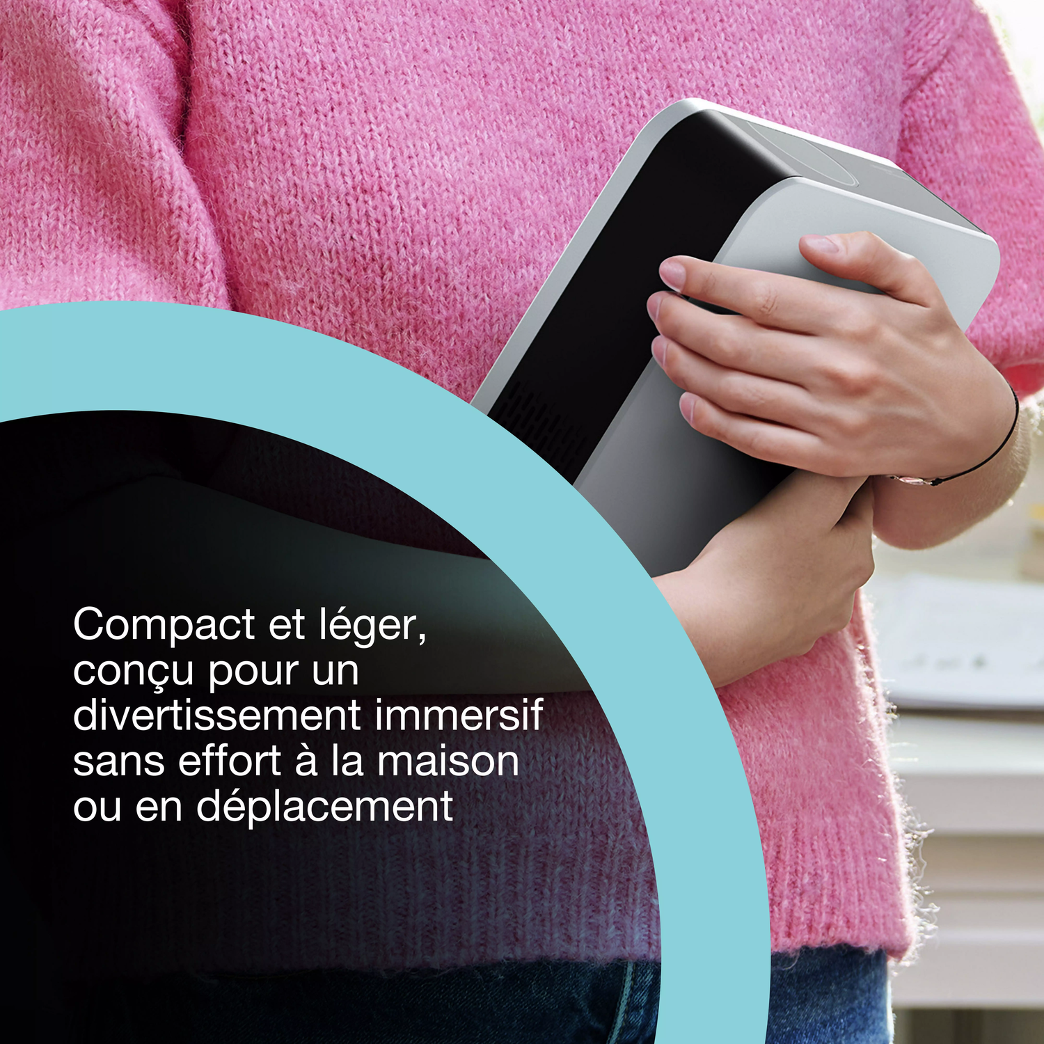 Une personne en pull rose tient un appareil gris et noir. Texte à gauche : Compact et léger, conçu pour un divertissement immersif.