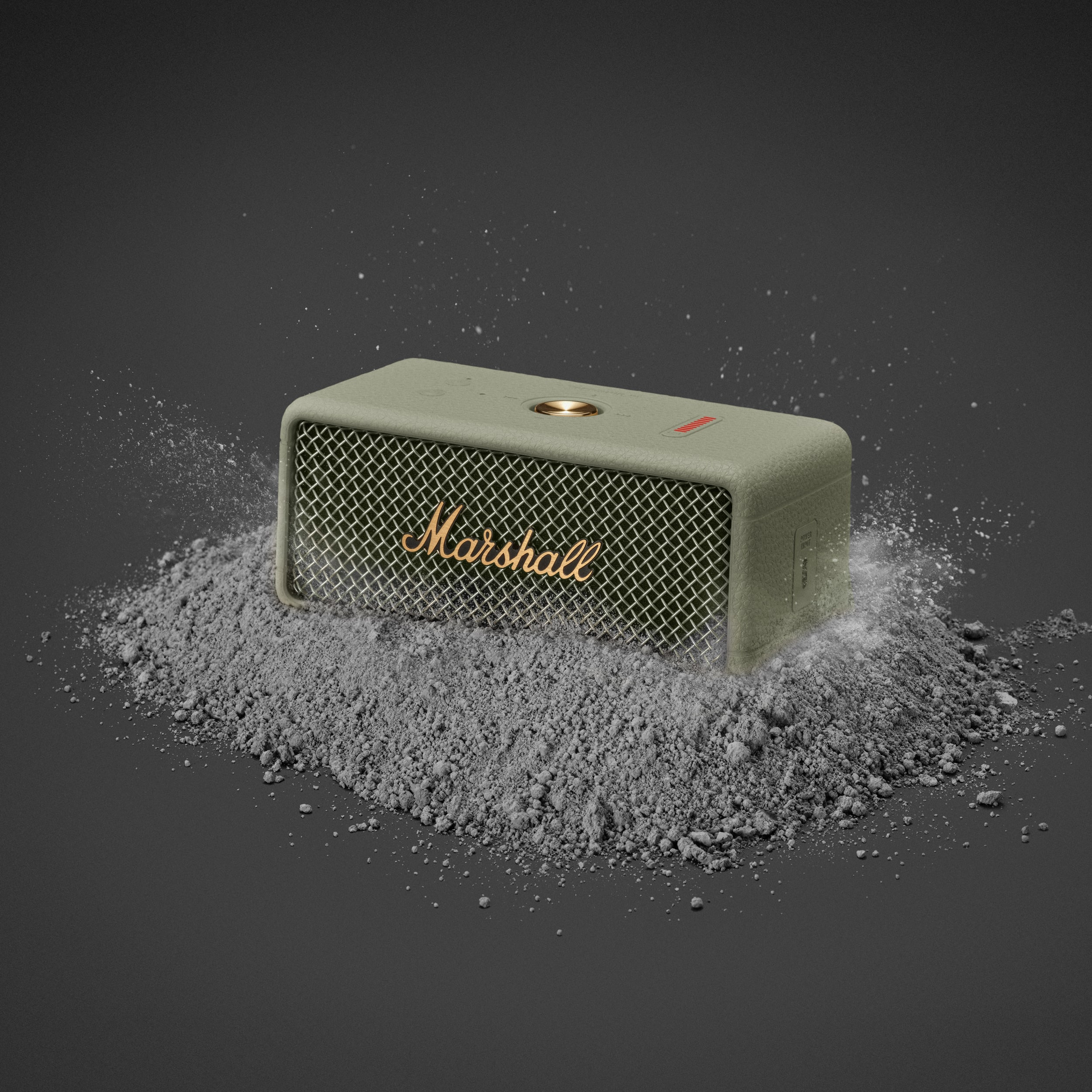 Ein Marshall-Lautsprecher steht auf grauem Pulver. Der Lautsprecher ist olivgrün und hat einen goldenen Regler und den Markennamen.