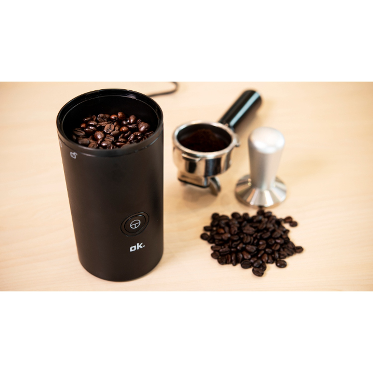 Macinacaffè nero con chicchi, portafiltro con caffè, pressino e mucchio di chicchi su superficie in legno.