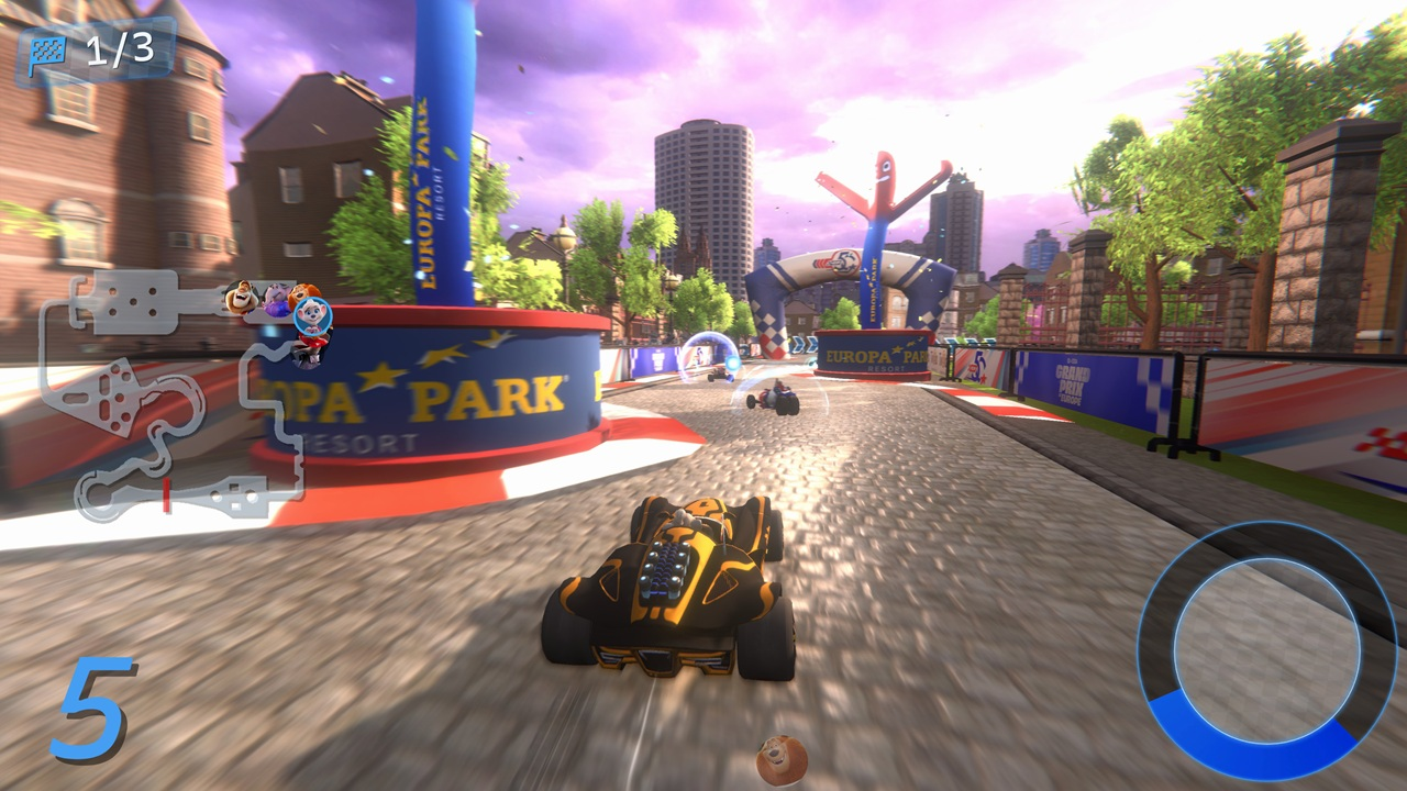 Un jeu de course de kart. Un kart noir et jaune est au premier plan. D'autres karts courent à l'arrière-plan. Des bâtiments et un ciel sont visibles.