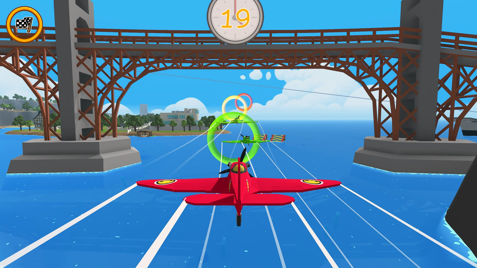 Un avion rouge vole à travers un anneau vert. En arrière-plan, un pont et le ciel.