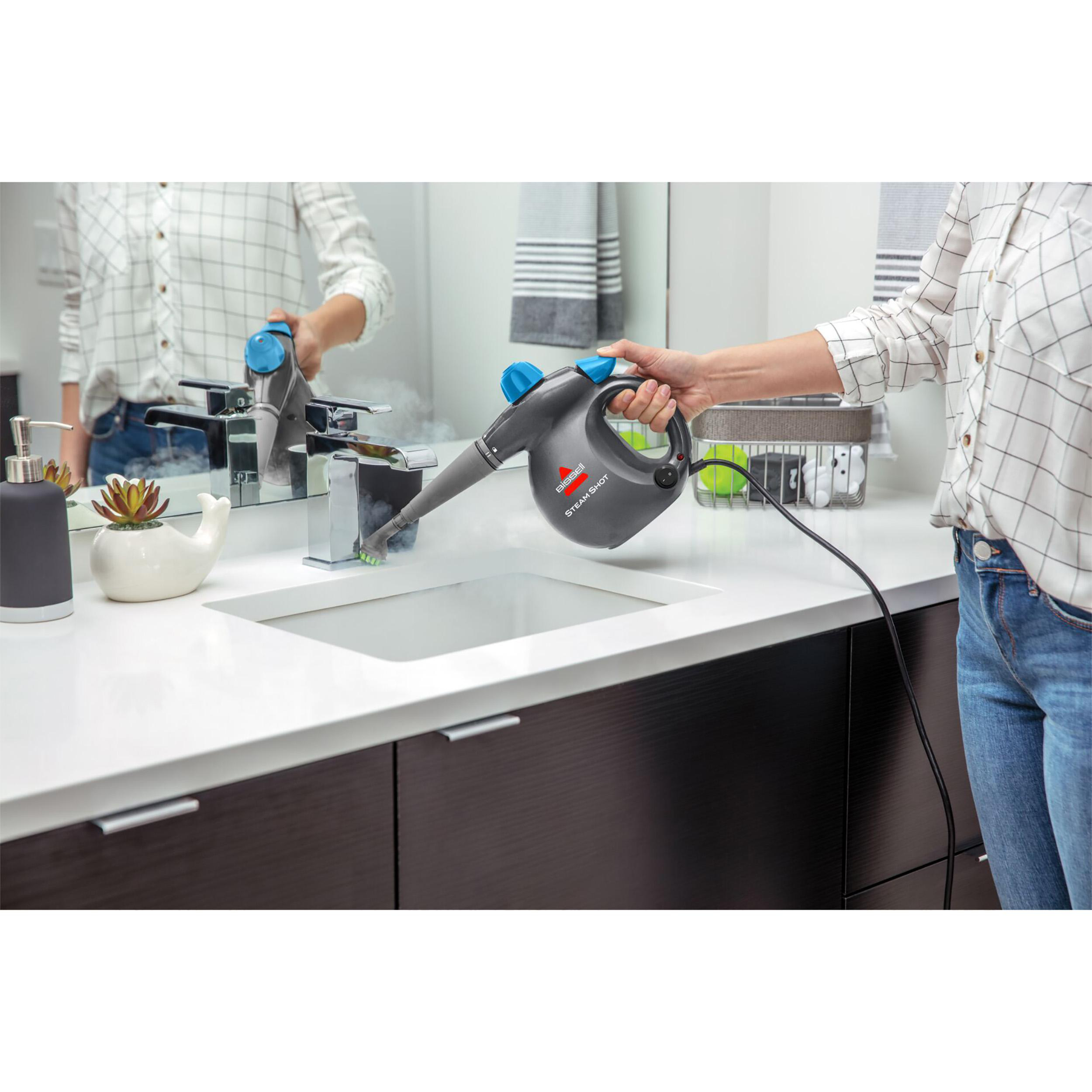 Eine Person dampft einen Wasserhahn mit einem Bissell Steam Shot. Die Szene ist ein Badezimmer mit Waschbecken.