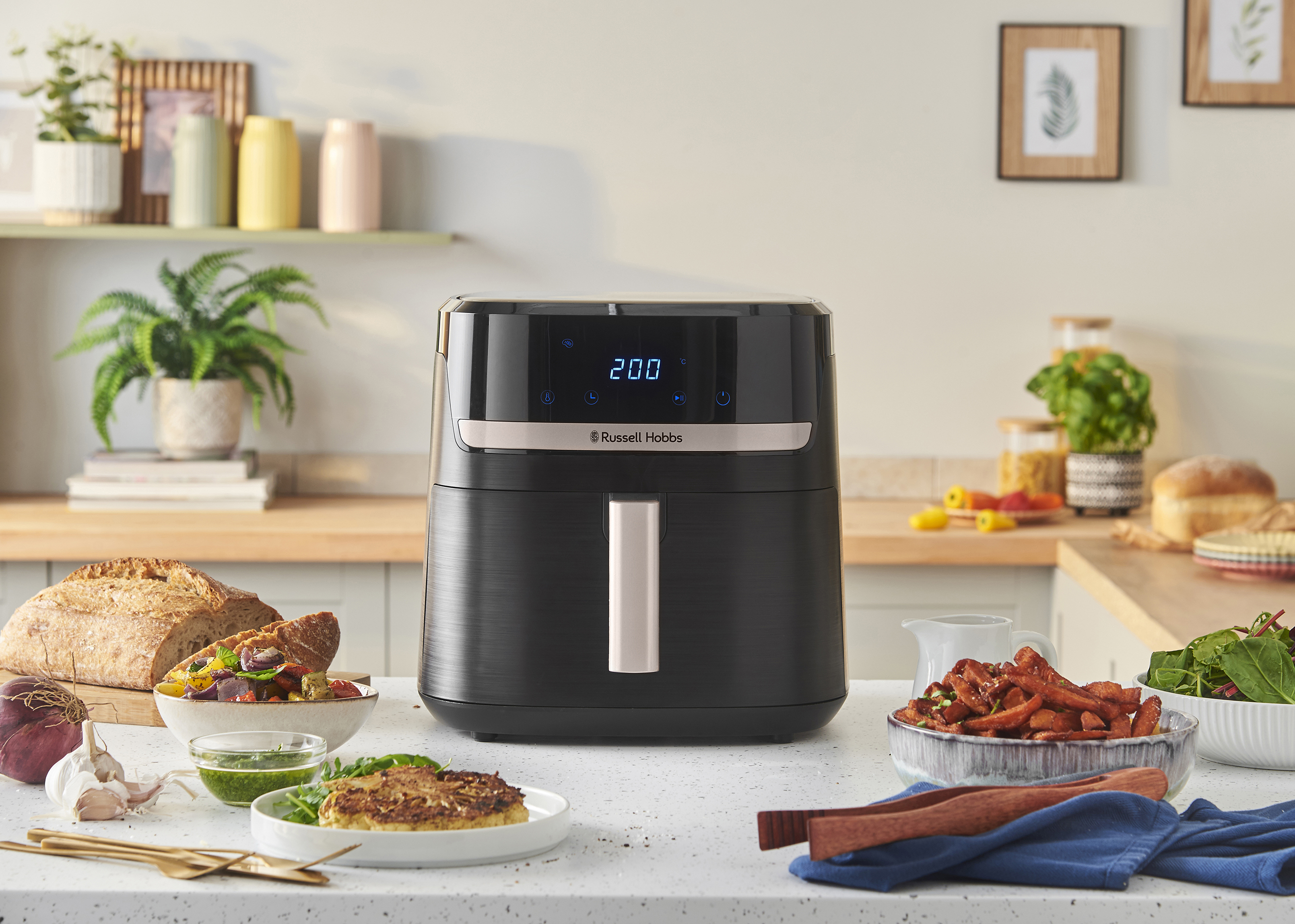 Egy air fryer a pulton ételekkel. Kenyér, zöldségek és édesburgonya-hasábburgonya is látható.