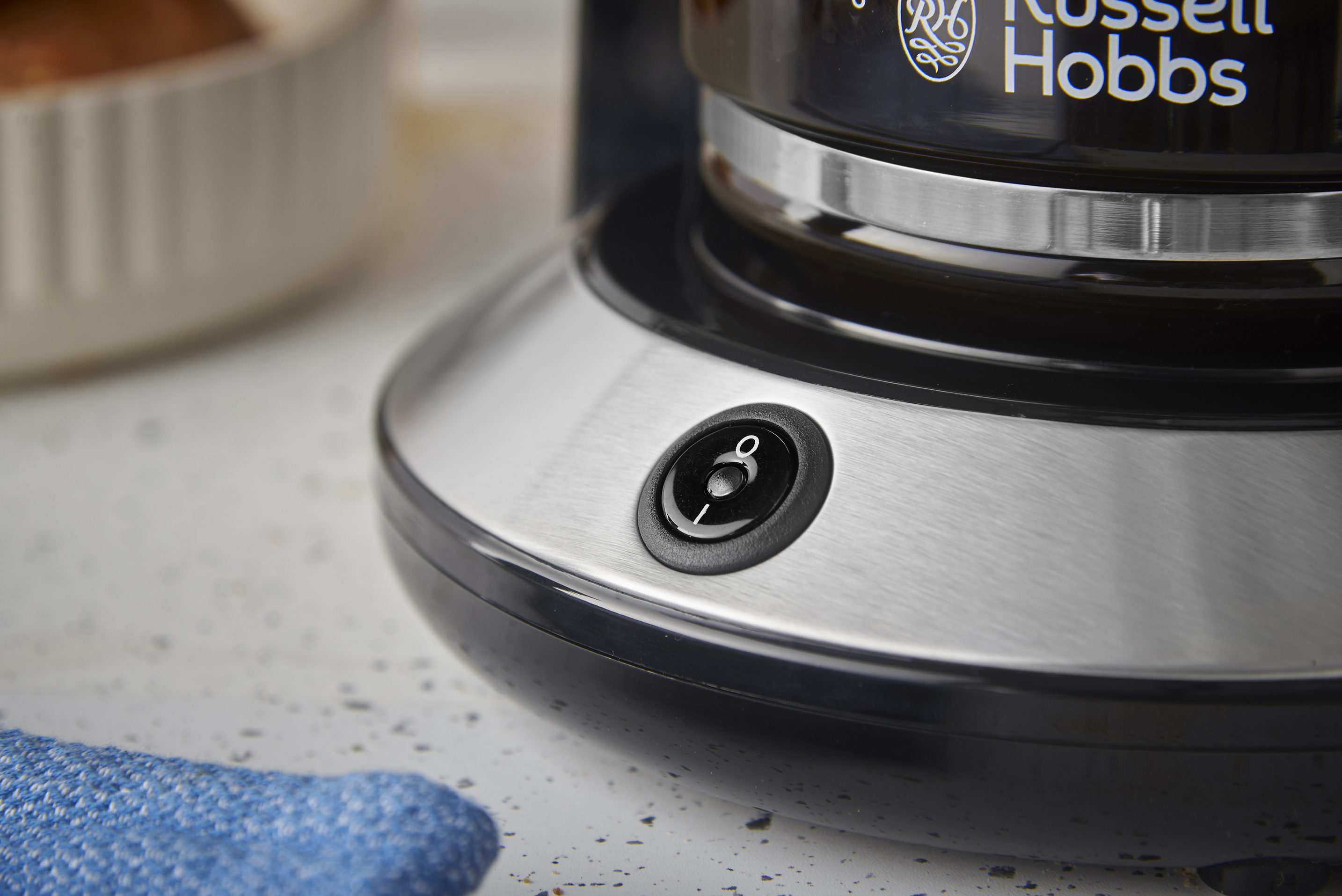 Közelkép egy Russell Hobbs kávéfőzőről. A bekapcsológomb látható. Egy kék rongy van a felületen.